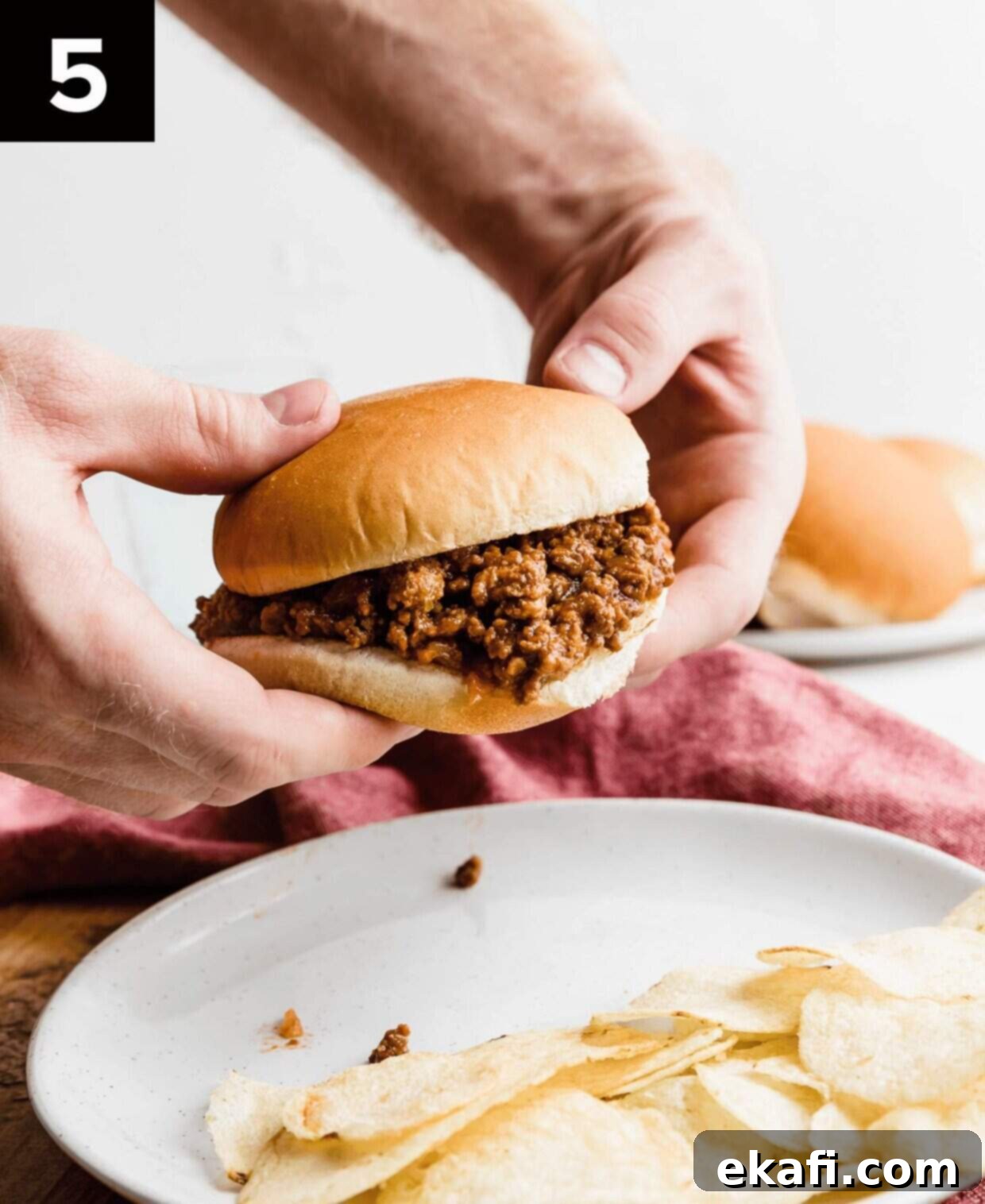 Hearty Old School Sloppy Joes 5 Two hands holding up a generously filled Homemade Sloppy Joe on a toasted bun, ready to be eaten.