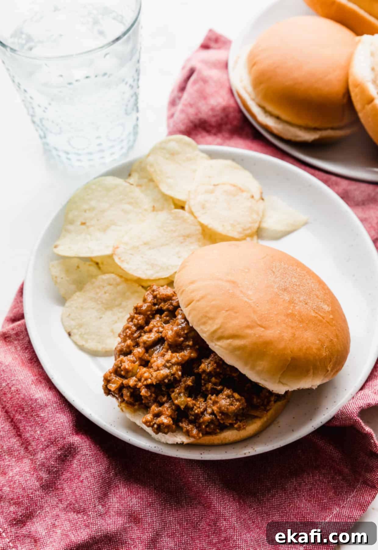 Hearty Old School Sloppy Joes 6 A delicious homemade sloppy Joe sandwich artfully presented on a white plate, accompanied by a generous serving of crispy potato chips.