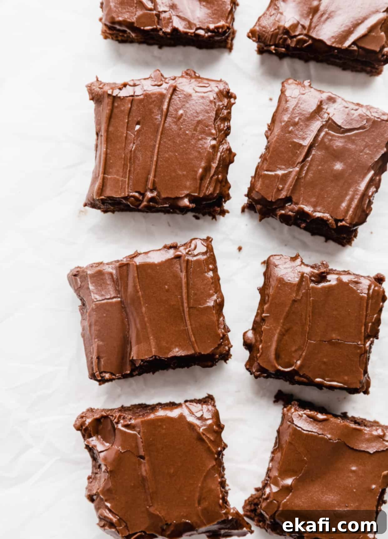 School Cafeteria Brownies 2 A row of frosting covered lunch lady brownies on a white background, showcasing their fudgy texture and shiny chocolate frosting.