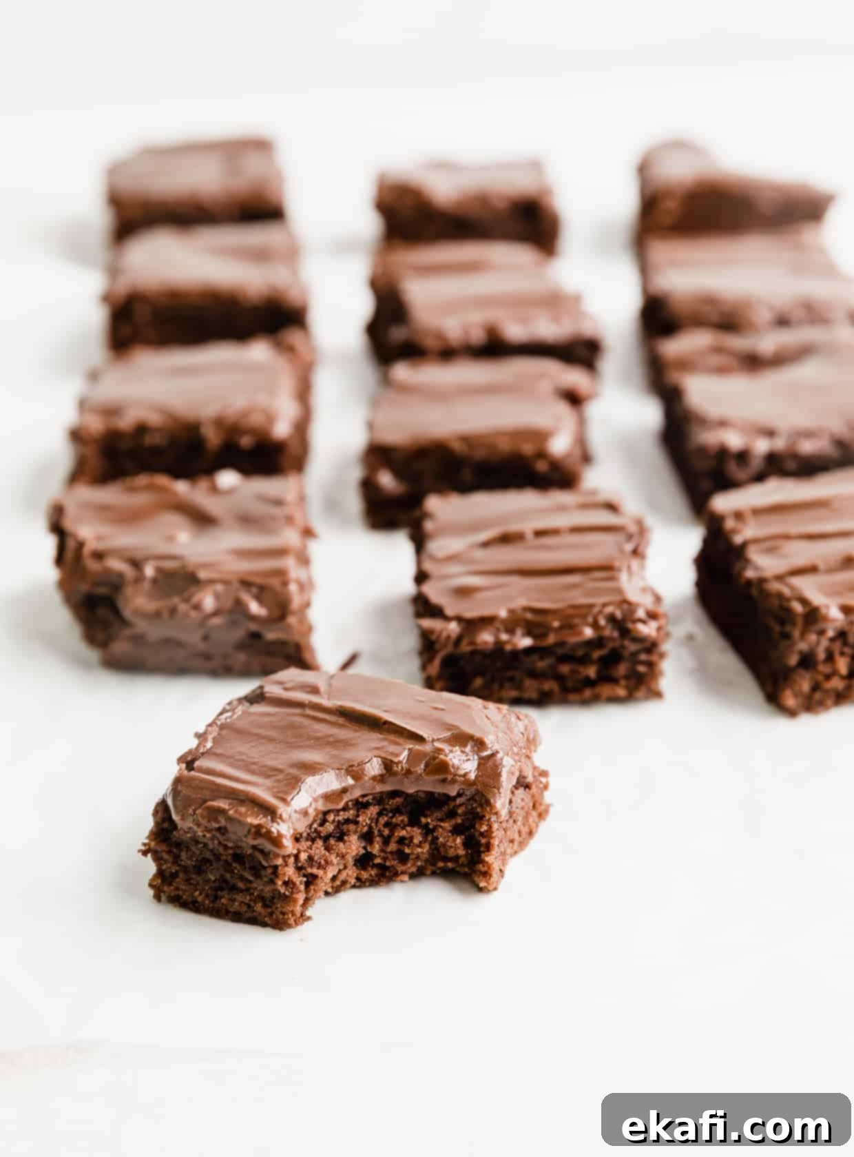 School Cafeteria Brownies 3 A close-up of a frosting covered lunch lady brownie with a bite taken out of it, revealing its dense, fudgy interior.