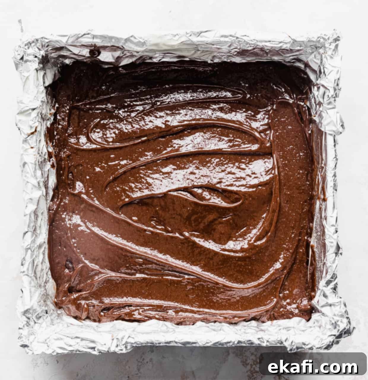 School Cafeteria Brownies 7 A foil-lined square brownie pan filled with raw chocolate brownie batter, spread evenly and ready for baking.