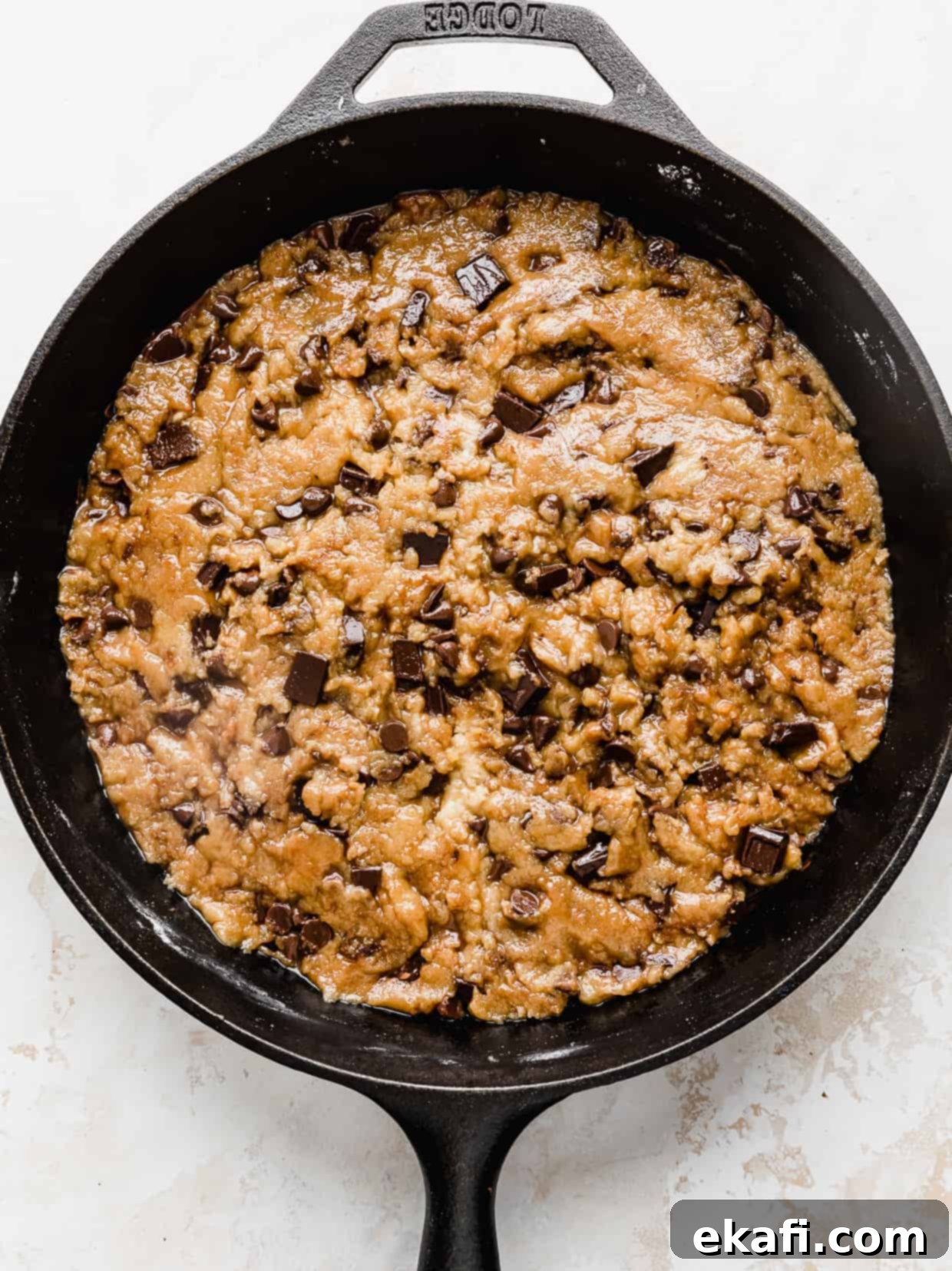Μπισκοτοπίτσα 9 Ένα άψητο pizookie (μπισκότο σοκολάτας τηγανιού) σε ένα μαντεμένιο τηγάνι με ένα ανάγλυφο λευκό φόντο.