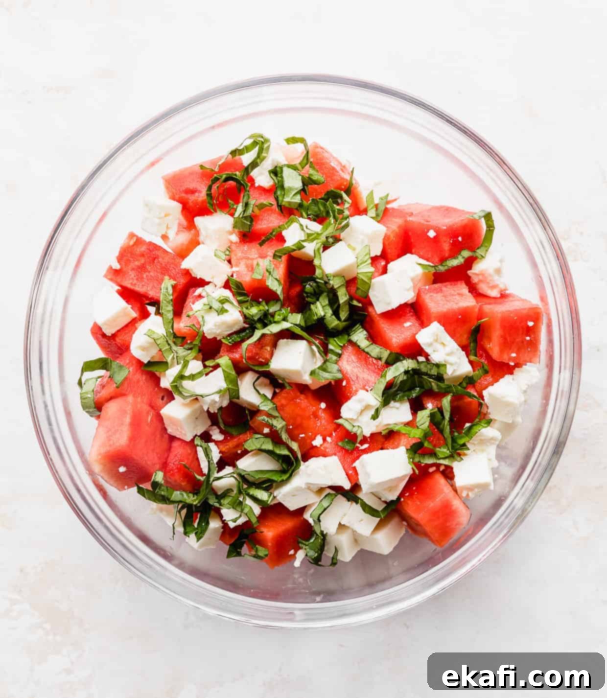 Watermelon Feta Basil Harmony 3 A clear glass bowl filled with colorful chopped watermelon, vibrant green basil, and creamy white feta cheese.