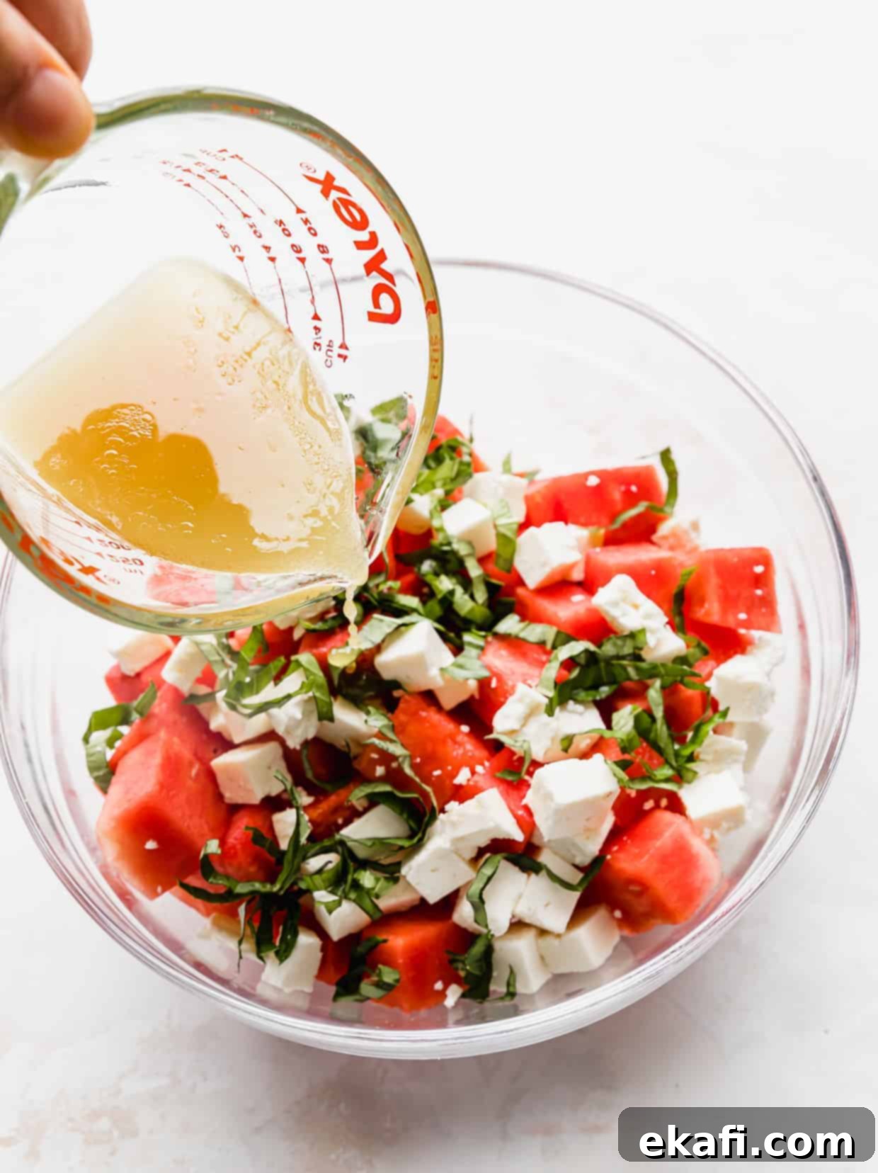 Watermelon Feta Basil Harmony 4 A light, golden dressing being poured over a Watermelon Feta Basil Salad in a clear glass bowl.