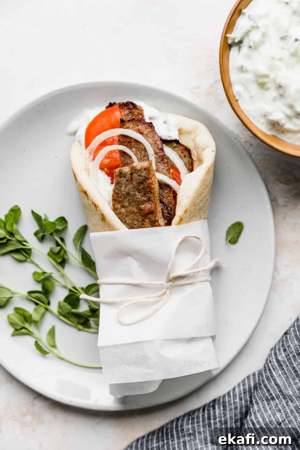 Mediterranean Lamb Gyros 2 A lamb gyro wrapped in white parchment paper on a white plate, showcasing the flavorful filling and fresh toppings.
