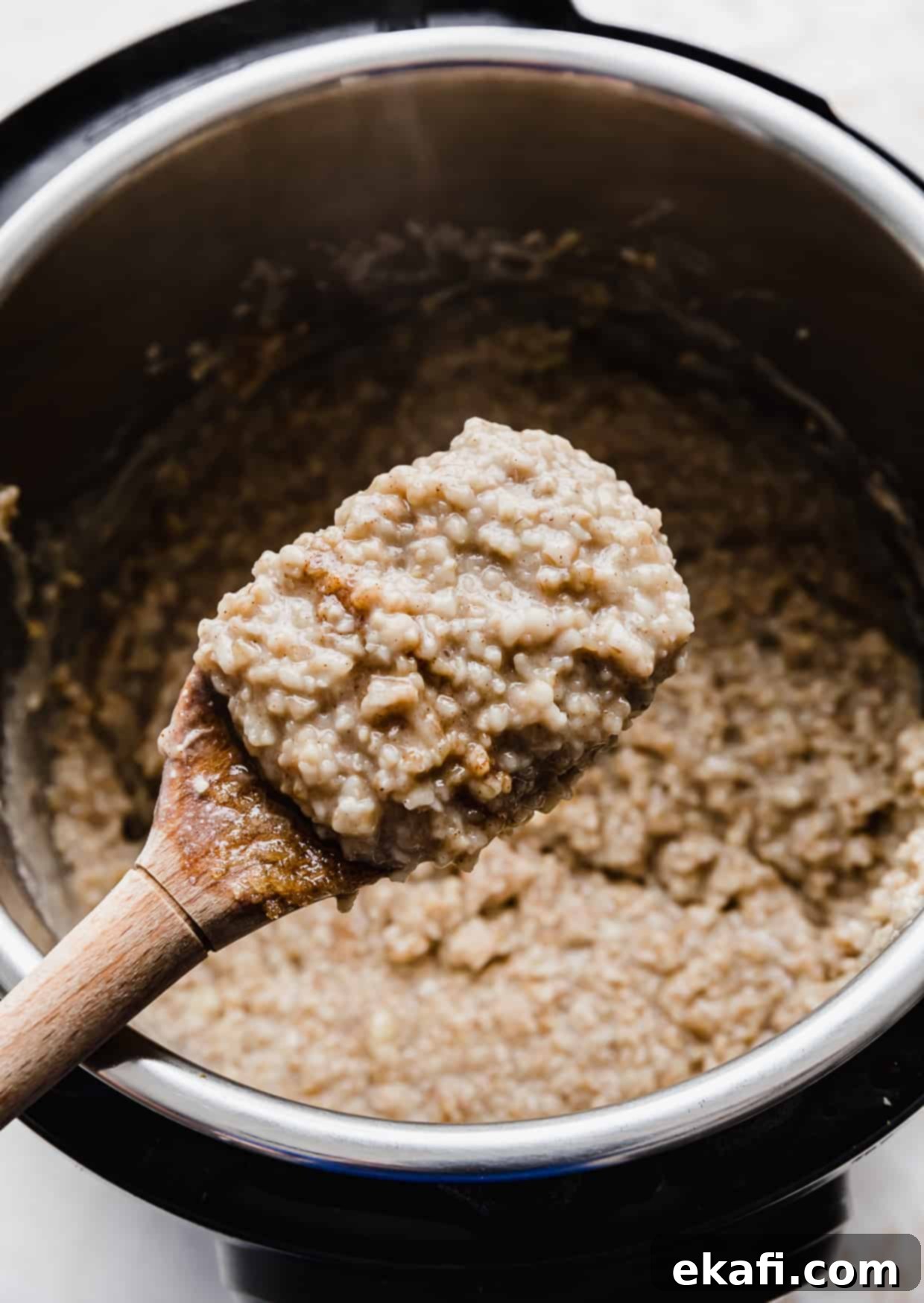 Banana Steel Cut Oat Delight 8 A wooden spoon holding up a spoonful of banana steel cut oats overtop of an instant pot, showcasing the creamy texture.