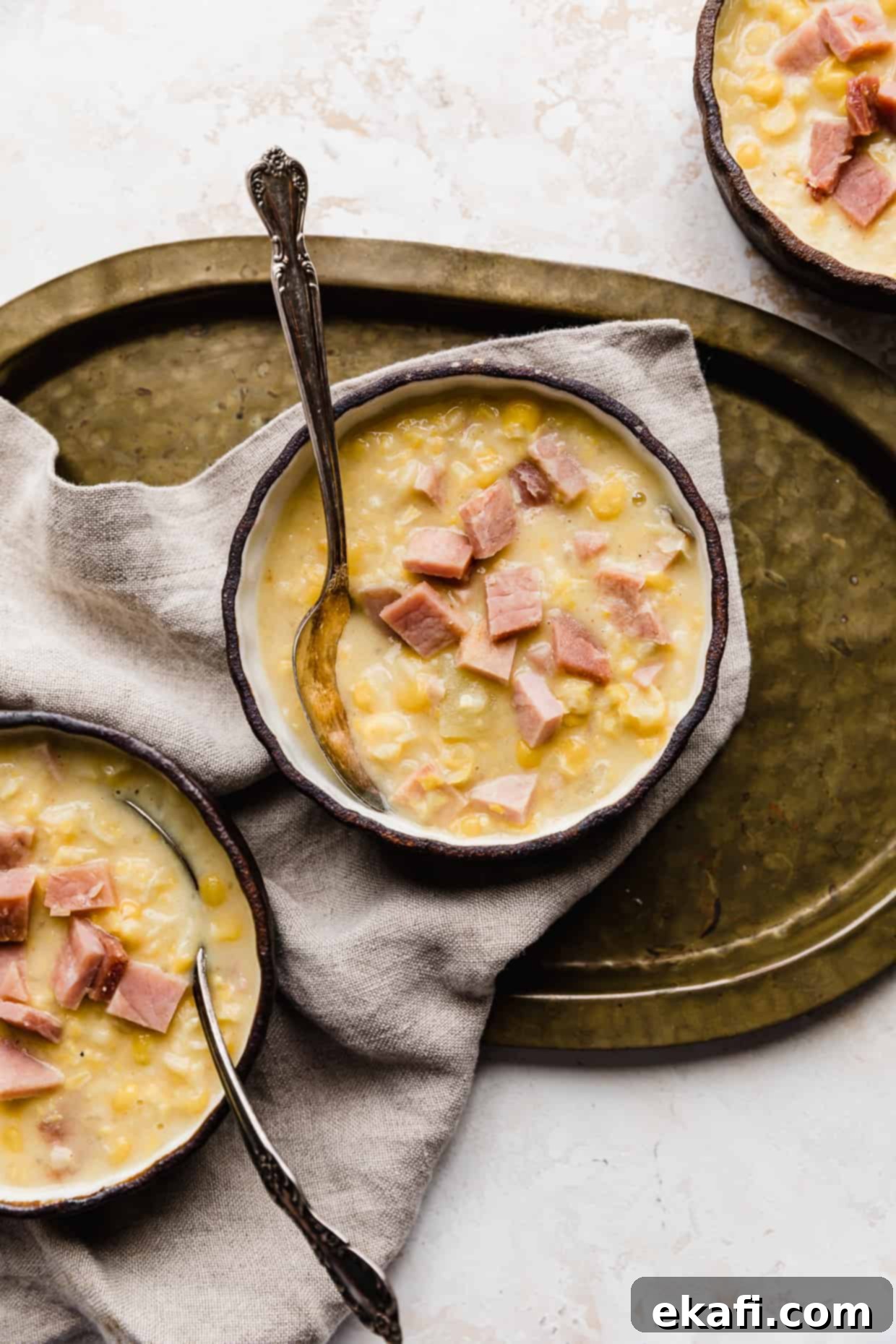 Hearty Ham and Sweet Corn Chowder 2 Three bowls of creamy Ham and Corn Chowder, with one bowl on a rustic bronze platter, garnished with fresh herbs.