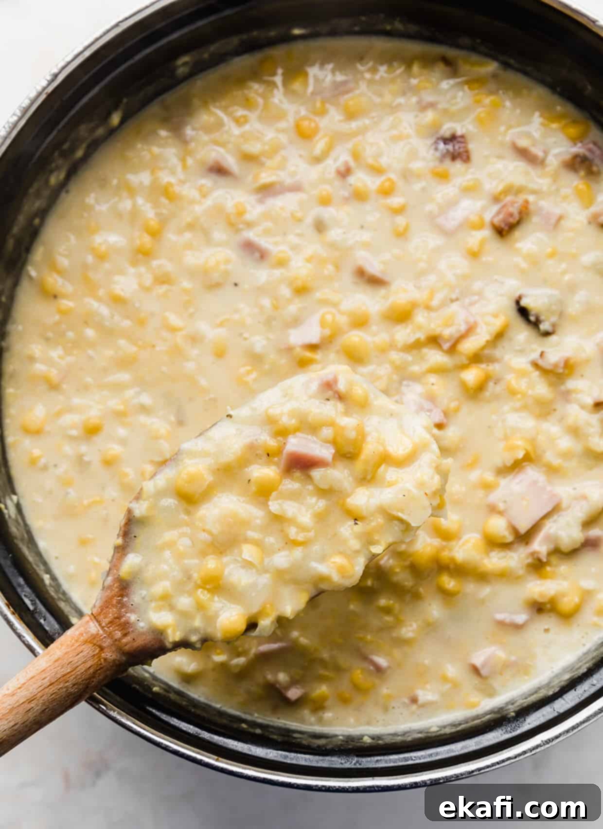 Hearty Ham and Sweet Corn Chowder 11 A wooden spoon scooping up a generous portion of homemade Ham and Corn Chowder from a black bowl, highlighting the creamy texture and chunks of ingredients.