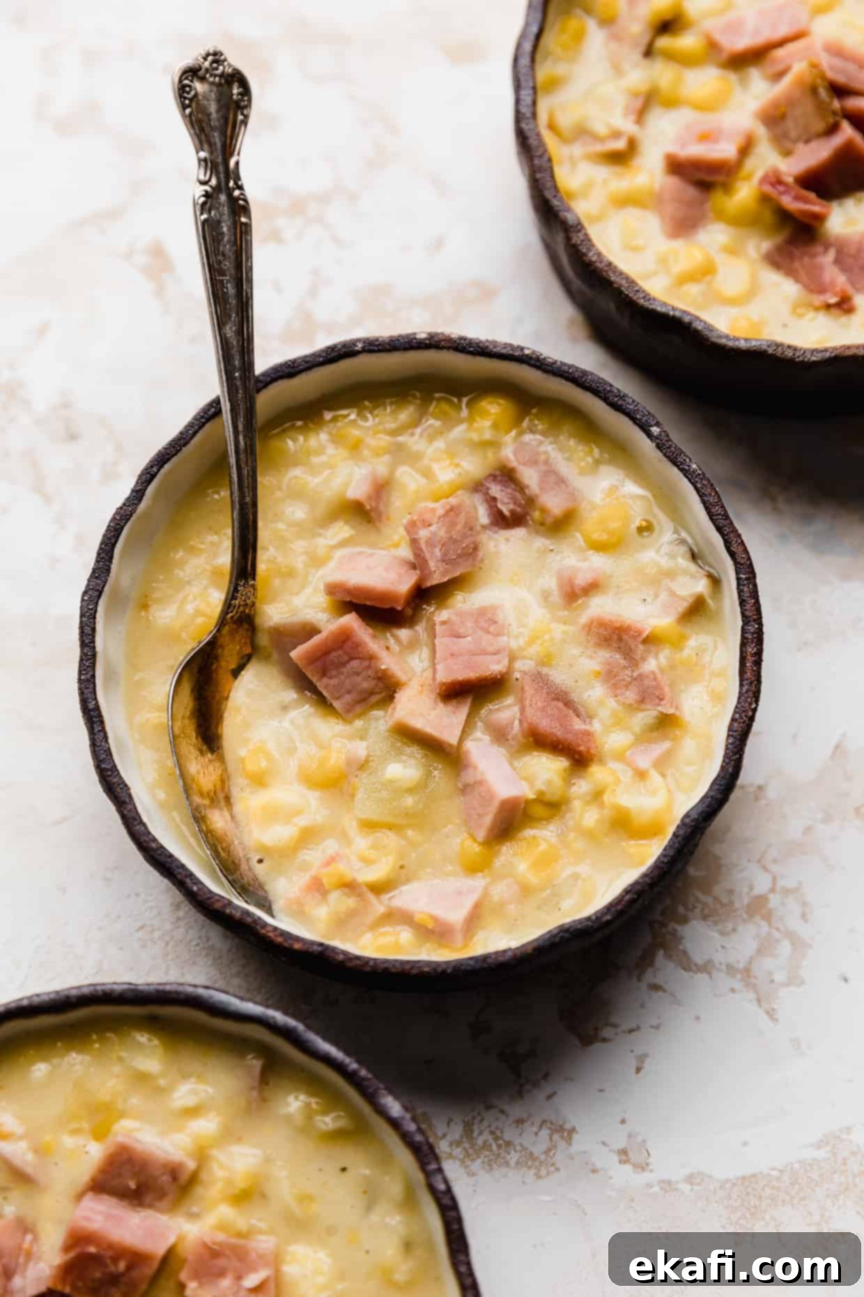 Hearty Ham and Sweet Corn Chowder 12 A close up of creamy Ham and Corn Chowder in a black bowl against a white textured background, ready to be enjoyed.