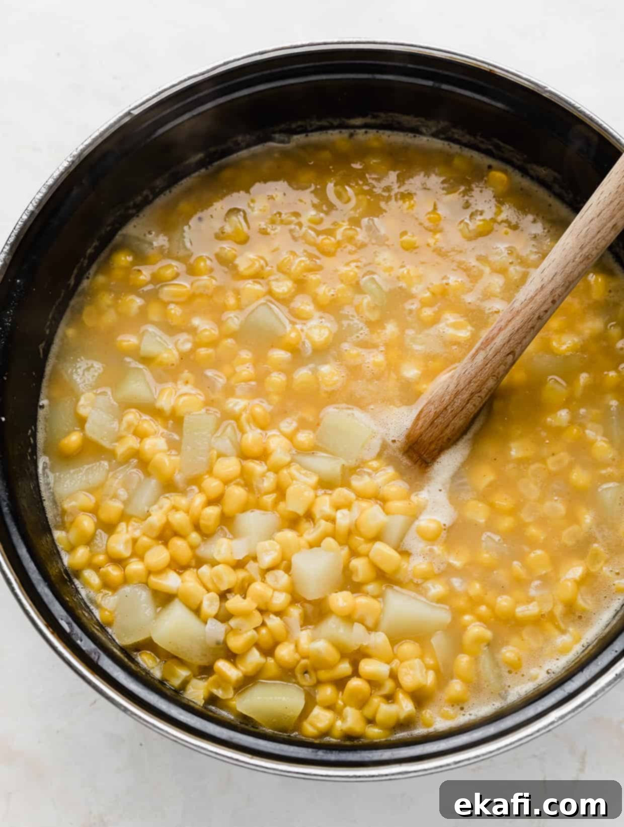 Hearty Ham and Sweet Corn Chowder 8 A wooden spoon stirring a large pot full of cooked corn and diced potatoes for ham and corn chowder.