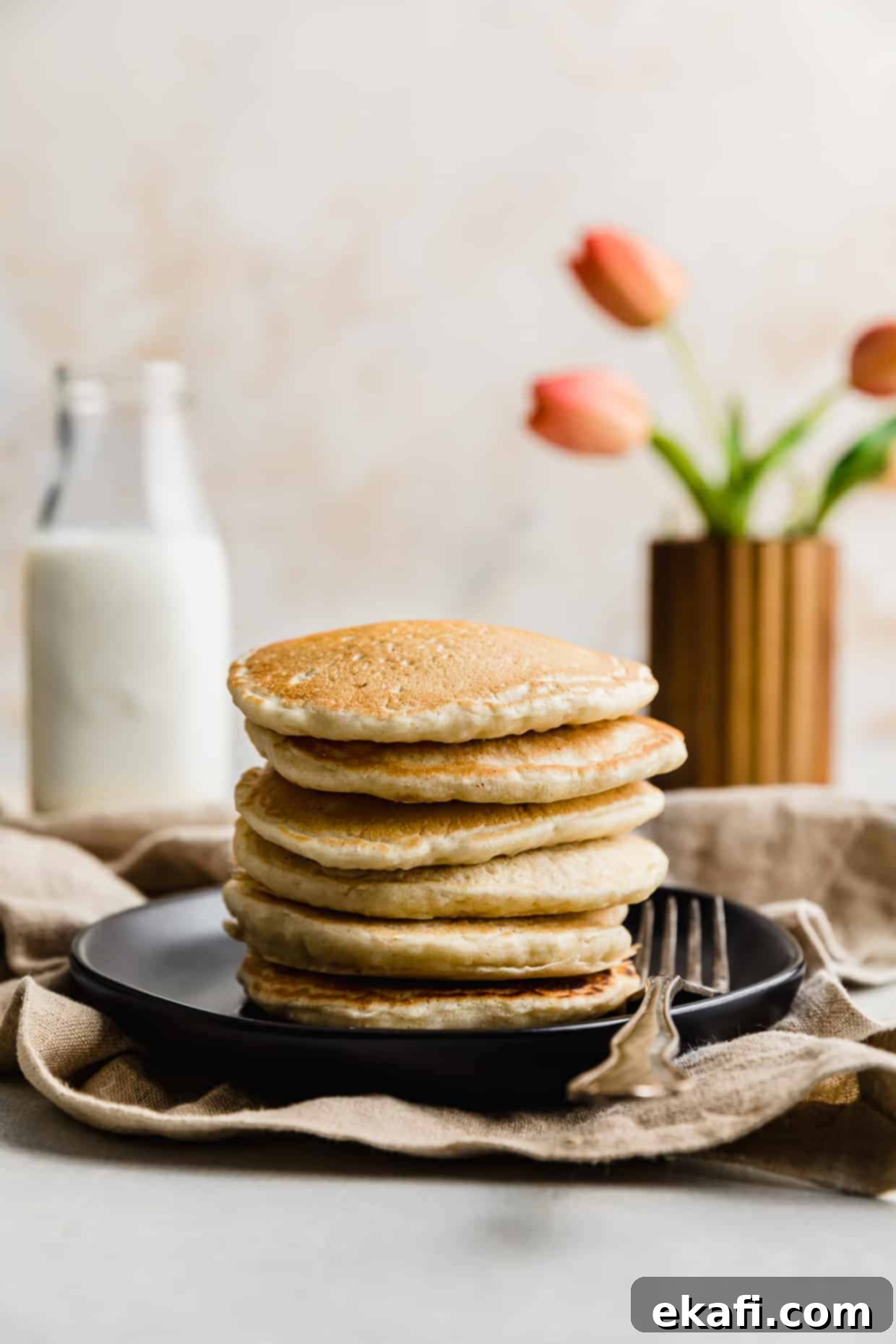 Fluffy Almond Milk Pancakes 2 A stack of Almond Milk Pancakes on a black plate with pink tulips in the background.