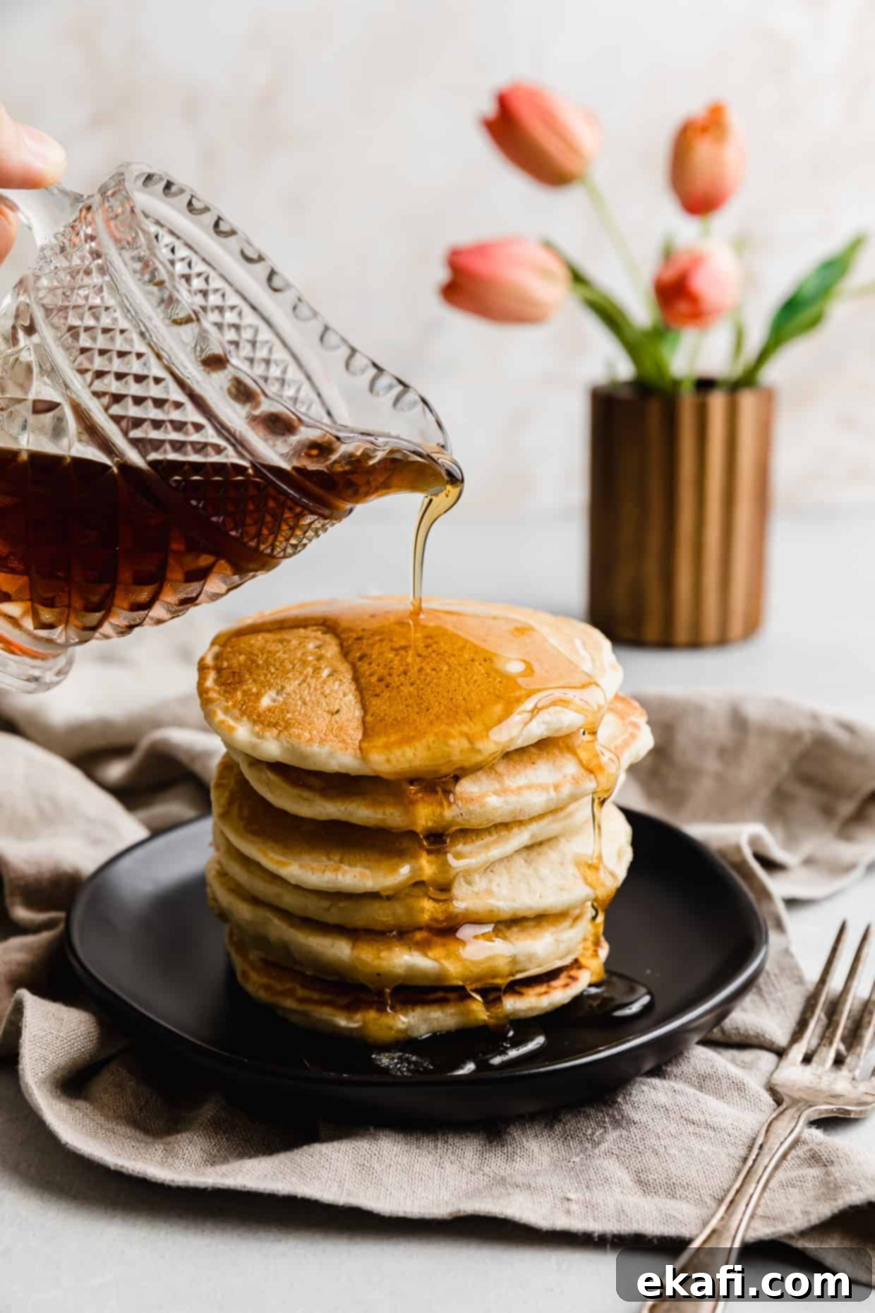 Fluffy Almond Milk Pancakes 11 Maple syrup being poured overtop of Almond Milk Pancakes on a black plate.