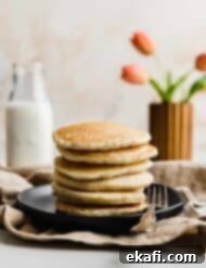 Fluffy Almond Milk Pancakes 13 A stack of Almond Milk Pancakes on a black plate with pink tulips in the background.