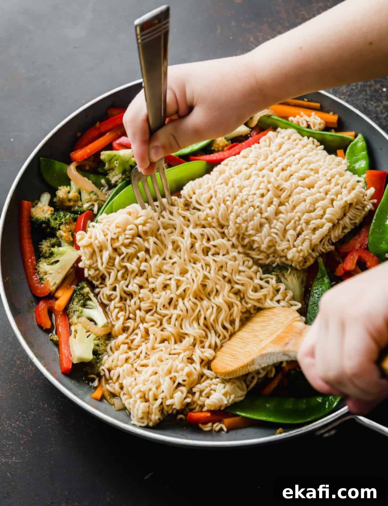 Ράμεν με Λαχανικά 11 Μαγειρεμένα νουντλς ramen σε ένα τηγάνι που διαχωρίζονται με ξύλινη κουτάλα και πιρούνι, ανακατεύοντας με τα λαχανικά.