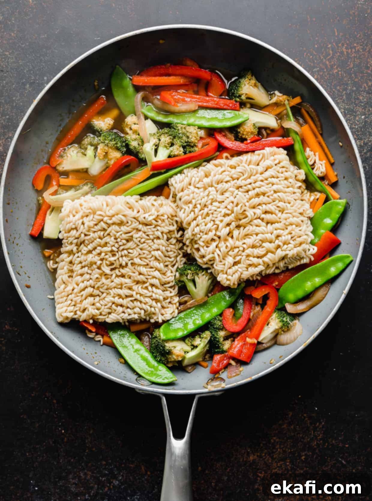 Ράμεν με Λαχανικά 10 Δύο δεσμίδες νουντλς ramen σε ένα τηγάνι πάνω από κομμένα λαχανικά, έτοιμα να απορροφήσουν τις γεύσεις.