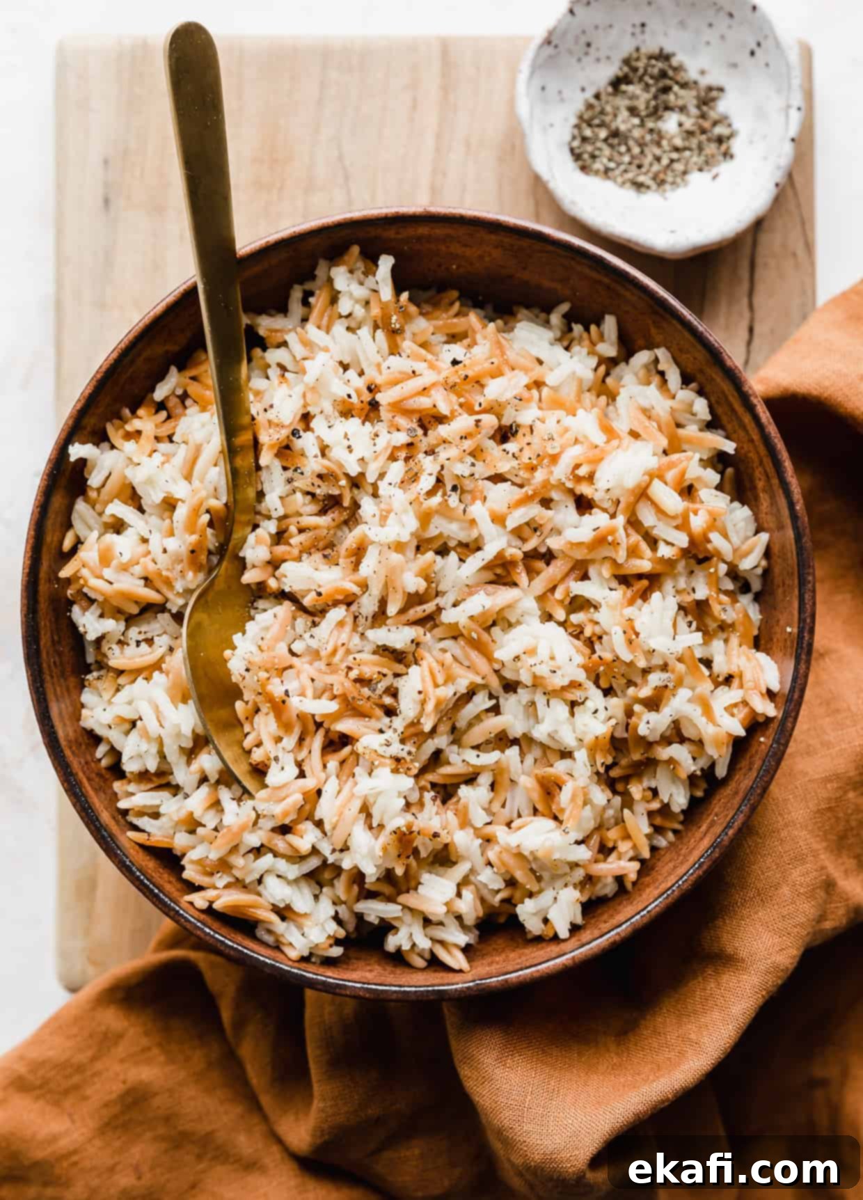 Orzo Pilaf 2 A large brown bowl filled with fluffy, golden Orzo Rice Pilaf, garnished with fresh herbs, resting on a wooden cutting board.