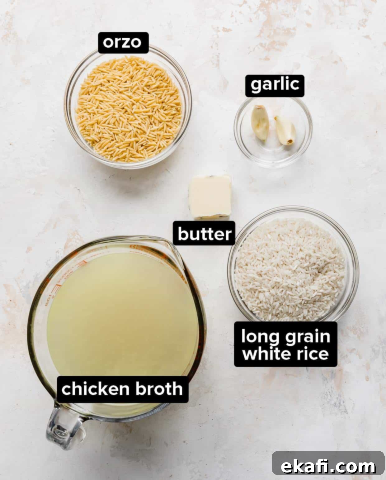 Orzo Pilaf 3 Fresh ingredients laid out for making Orzo Rice, including butter, garlic cloves, dry orzo pasta, long grain white rice, and chicken broth.