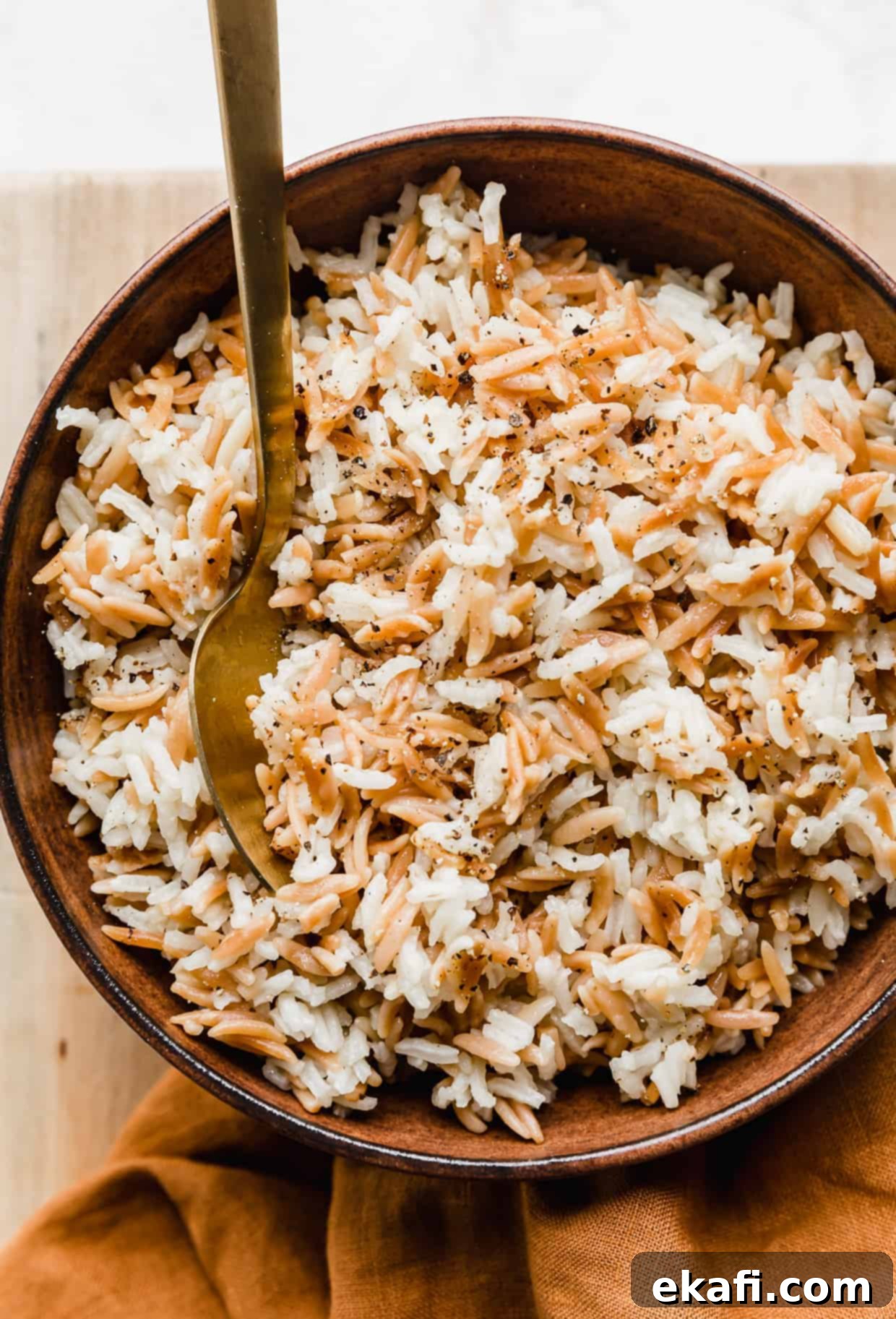 Orzo Pilaf 9 A golden spoon poised in a large brown bowl, brimming with a generous serving of perfectly cooked Orzo Rice Pilaf, ready to be enjoyed.