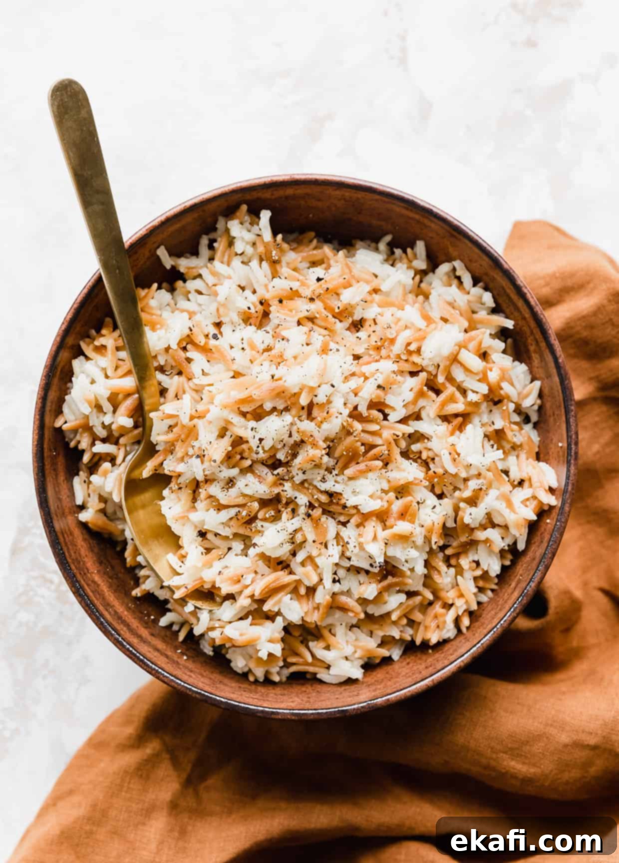 Orzo Pilaf 10 Orzo rice pilaf served in a rustic brown bowl, with a golden spoon resting inside, highlighting its fluffy texture.