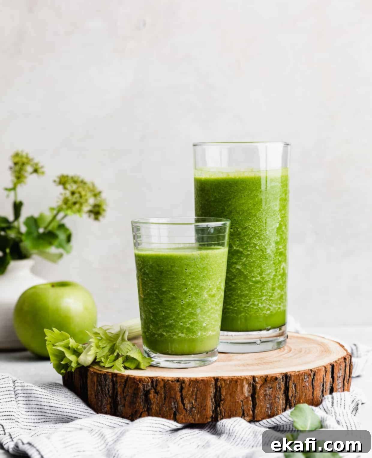 Green Celery Smoothie 8 Two glasses full of dark green celery smoothie on a wooden round board.