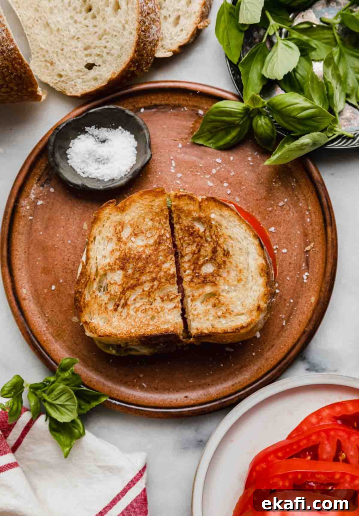 Pesto Mozzarella Sandwich 5 Pesto Mozzarella Sandwich on a brown plate, sliced in half with fresh basil in a bowl at the right corner of the photo.