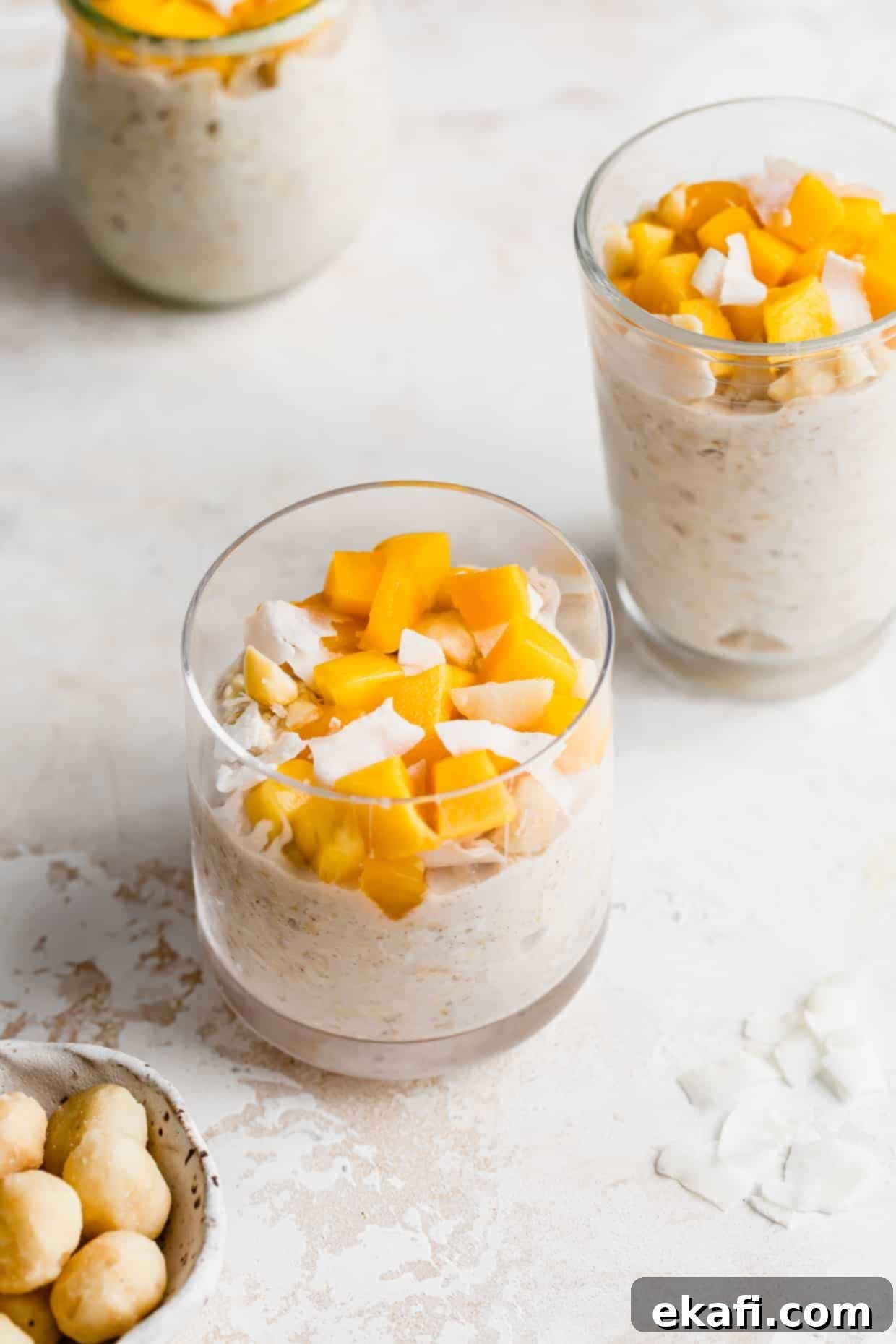 Dreamy Mango Overnight Oats 2 A clear cup full of Mango Overnight Oats topped with diced mangos and shaved coconut flakes.