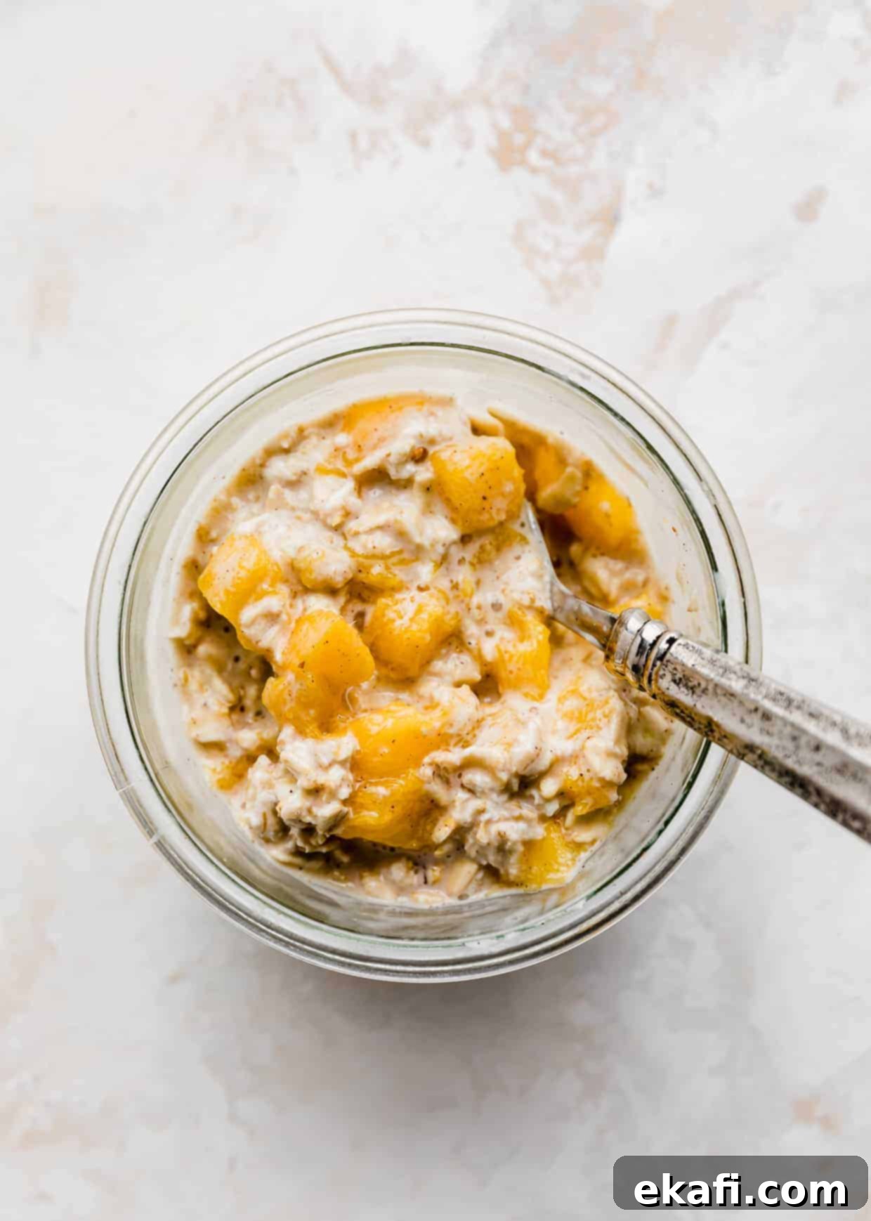 Dreamy Mango Overnight Oats 3 Overhead photo of a spoon scooping into mango overnight oats with cinnamon and nutmeg.