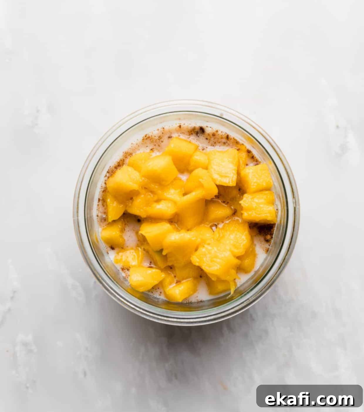 Dreamy Mango Overnight Oats 8 Diced mango overtop of a milk and oat mixture in a glass jar.