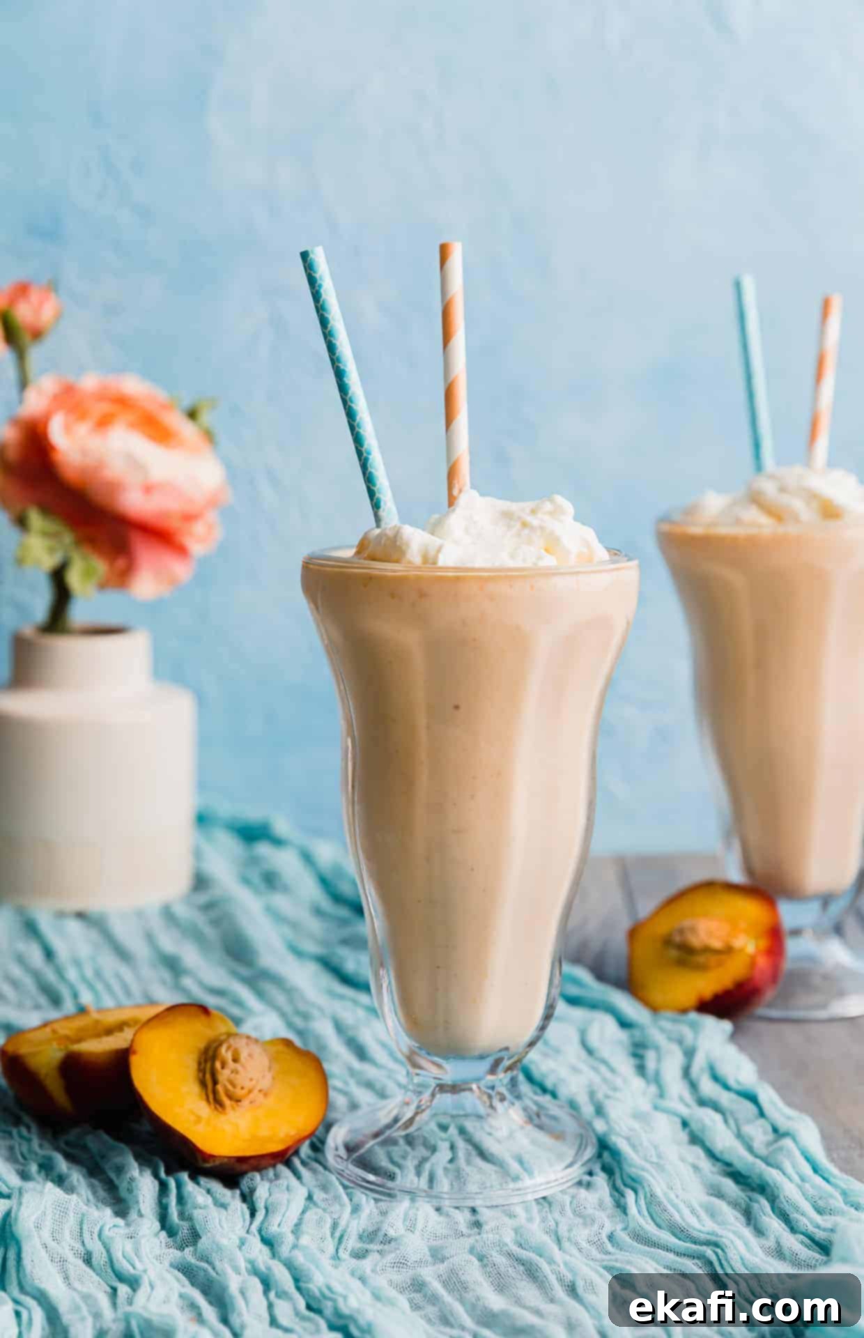 Velvet Peach Shake 2 Two glasses of creamy homemade peach milkshake topped with whipped cream against a soft blue background, showcasing a perfect summer dessert.
