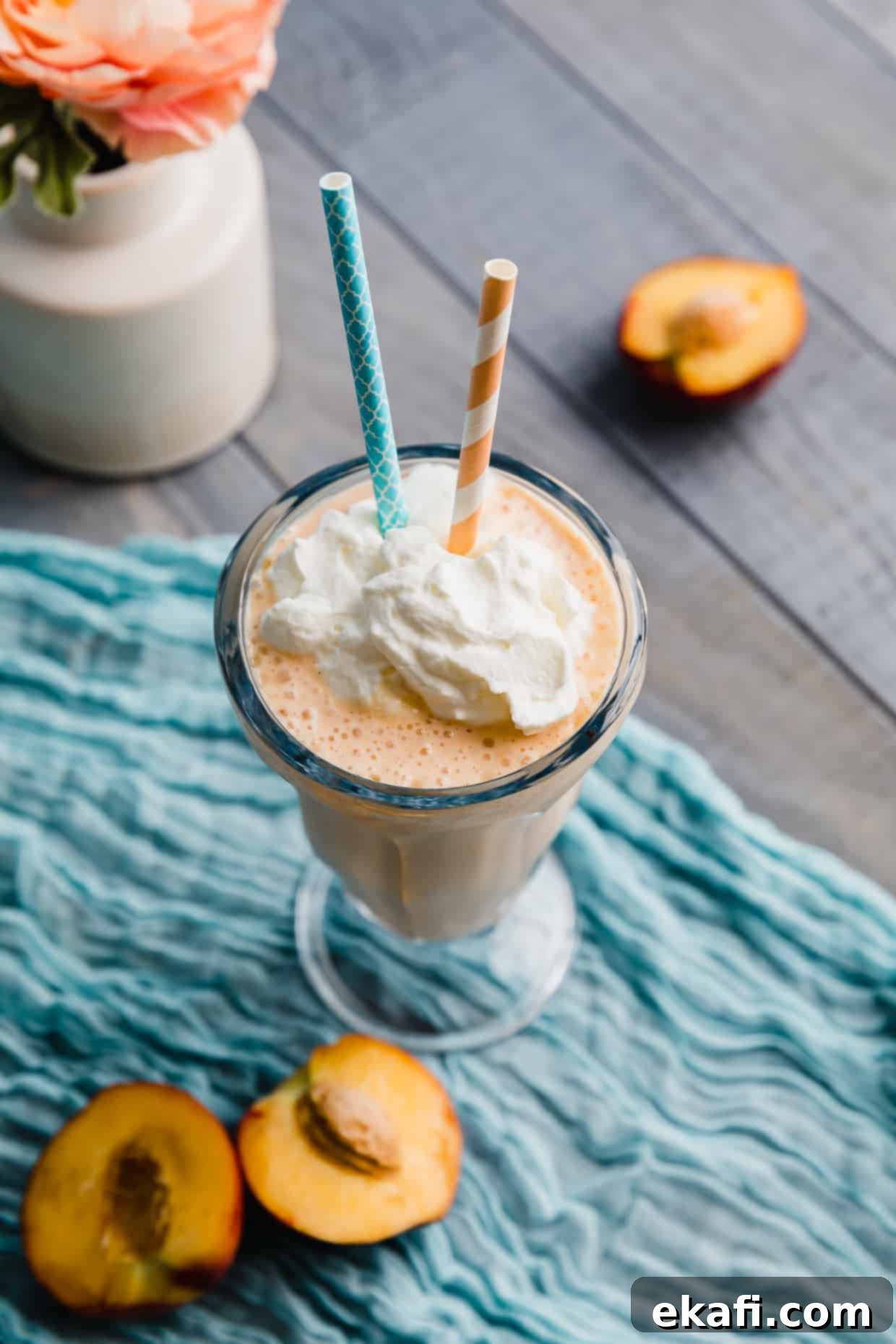 Velvet Peach Shake 6 A beautifully presented peach milkshake in a glass, with a blue napkin and two straws, ready to be enjoyed.