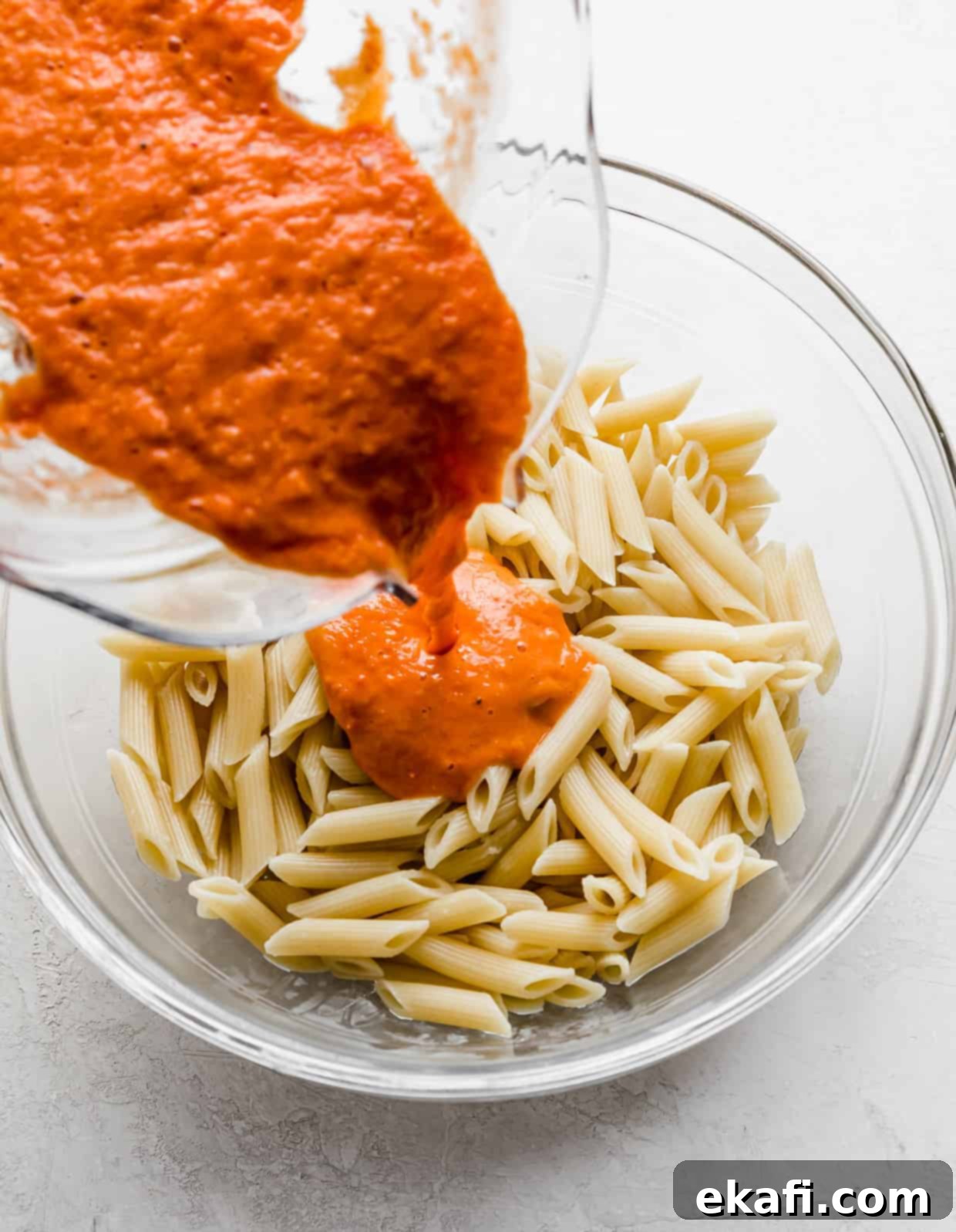 Perfect Penne Pomodoro 6 Fresh pureed tomato sauce being poured overtop cooked penne noodles in a clear glass bowl, showcasing the rich color.