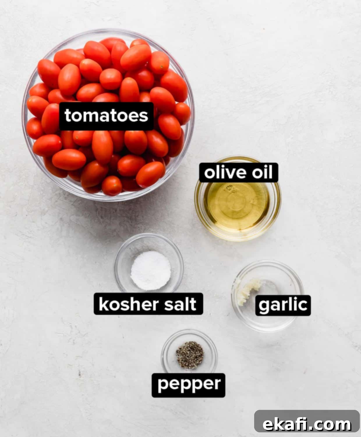 Blistered Grape Tomatoes 3 Ingredients used to make roasted tomatoes, including grape tomatoes, olive oil, garlic, salt, and pepper, arranged on a gray background.