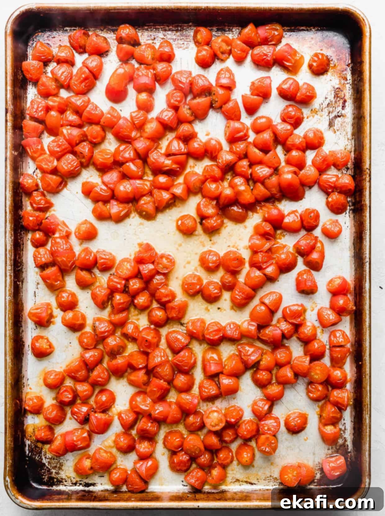 Blistered Grape Tomatoes 8 Shriveled and beautifully roasted small red tomatoes on a baking sheet, showcasing their concentrated texture.