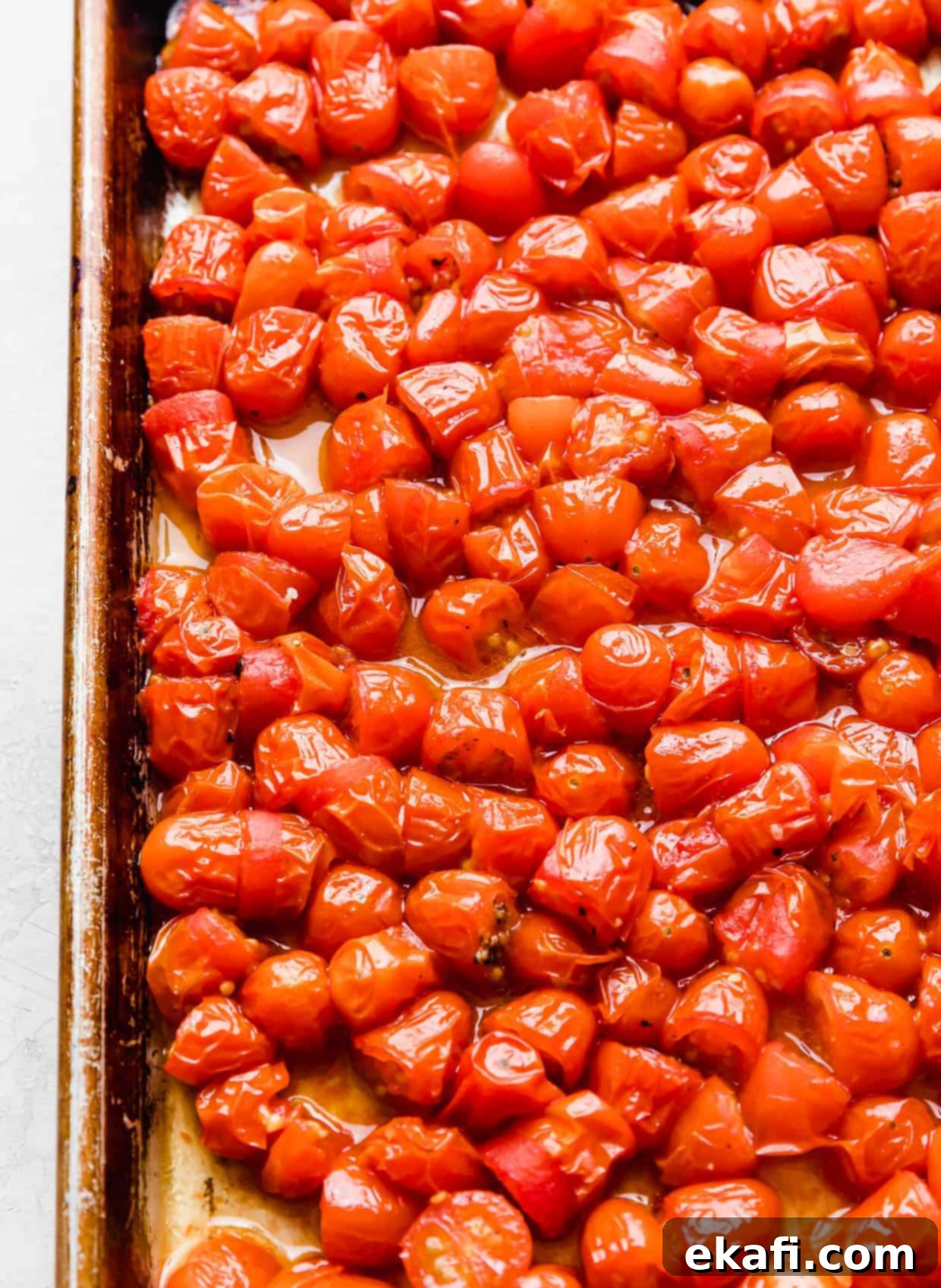 Blistered Grape Tomatoes 9 Roasted small red tomatoes, some cut in half, on a baking sheet, showcasing their tender texture and concentrated juices.