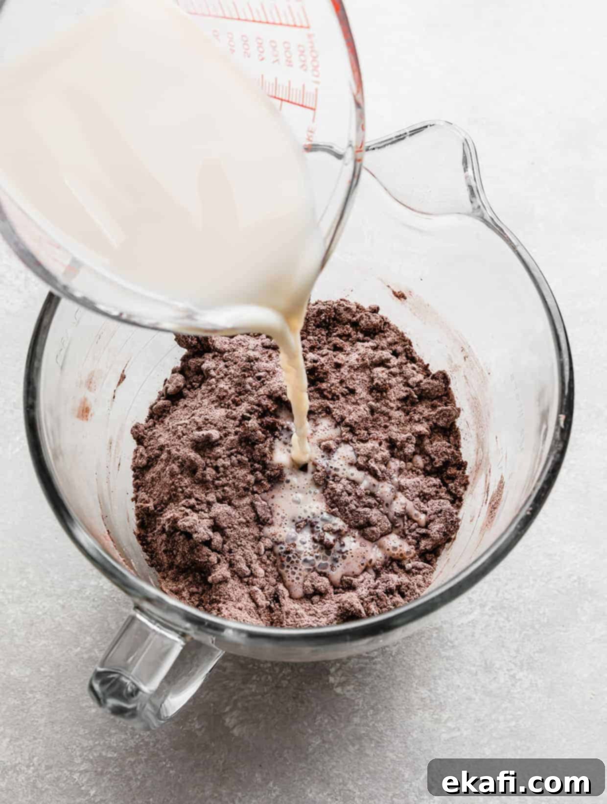 Chocolate Peanut Butter Symphony 6 A white liquid mixture being poured into a bowl containing chocolate cake dry ingredients and butter, illustrating the combination of wet and dry components.