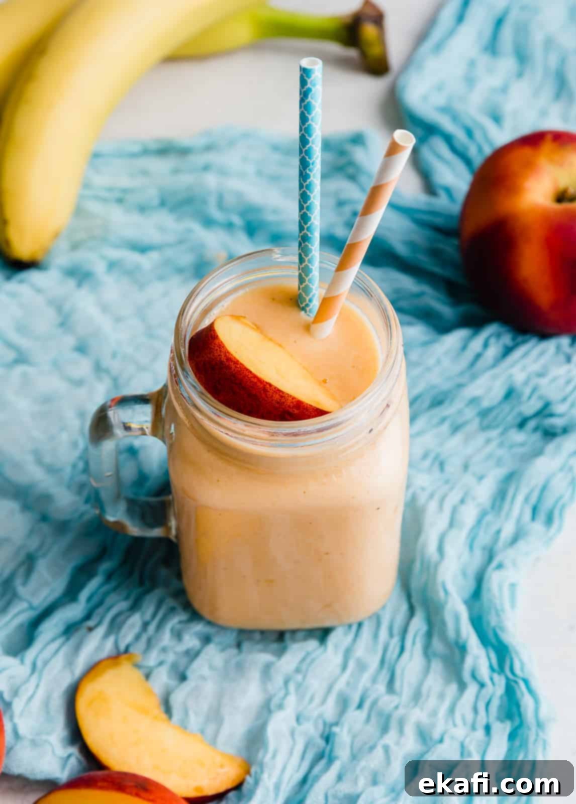 Creamy Peach Banana Bliss 2 A glass cup filled with a banana peach smoothie topped with a slice of fresh peach.