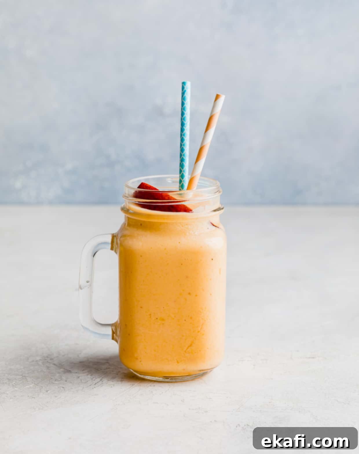 Creamy Peach Banana Bliss 3 A glass cup filled with an orange colored peaches and banana smoothie against a light blue background.
