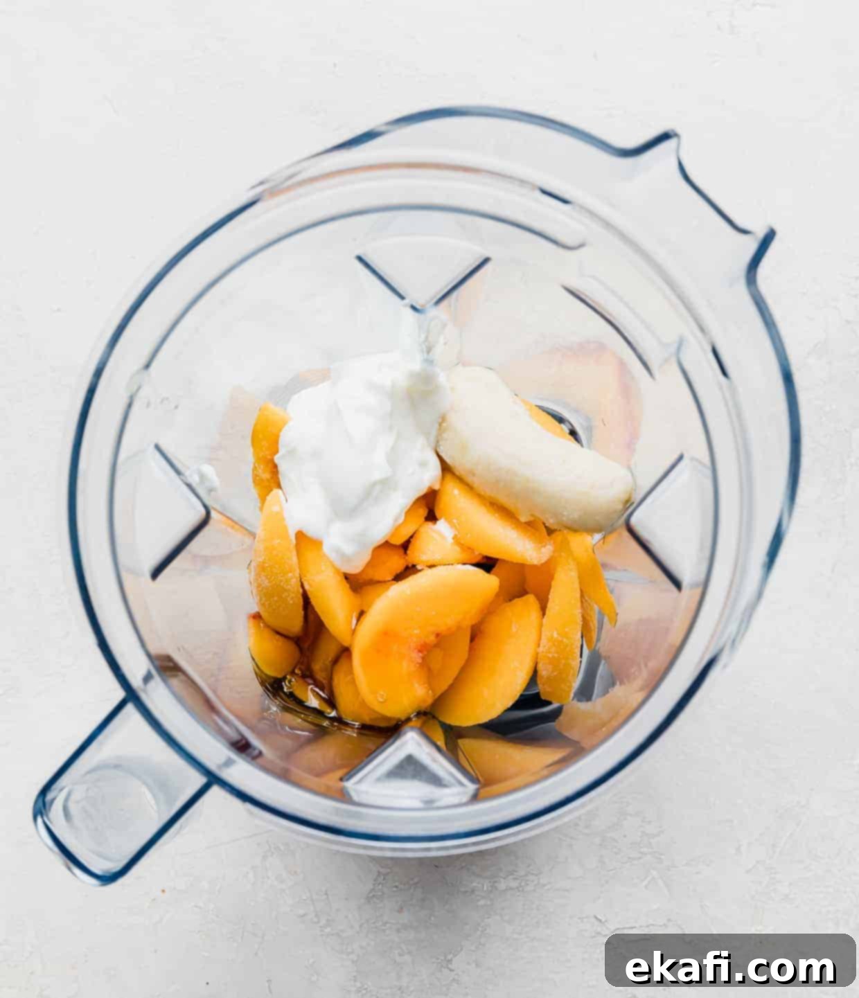 Creamy Peach Banana Bliss 5 Overhead photo of a blender filled with frozen peach slices, yogurt, banana, milk, and honey.