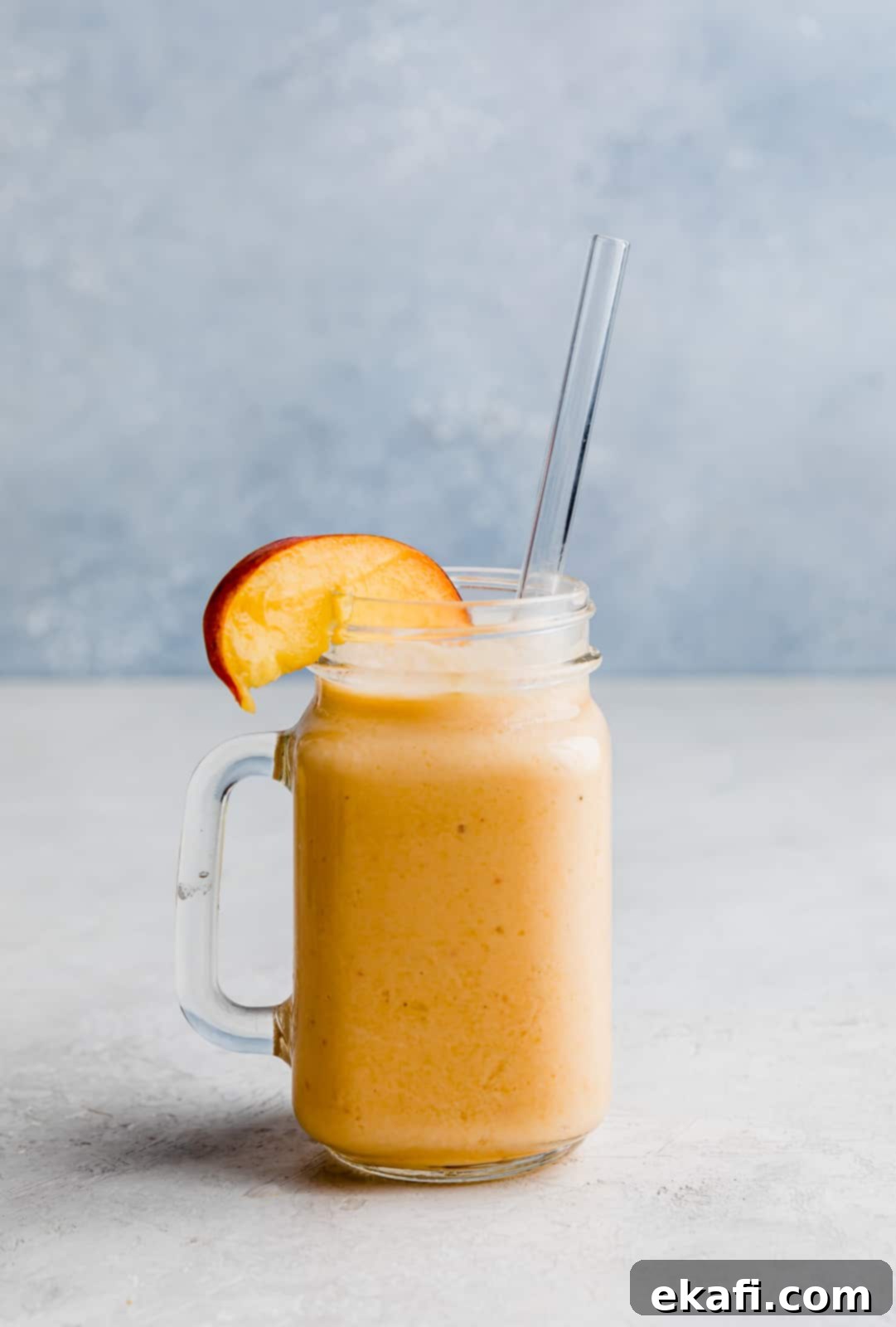 Creamy Peach Banana Bliss 8 A banana peach smoothie in a glass cup with a fresh peach slice on the rim.