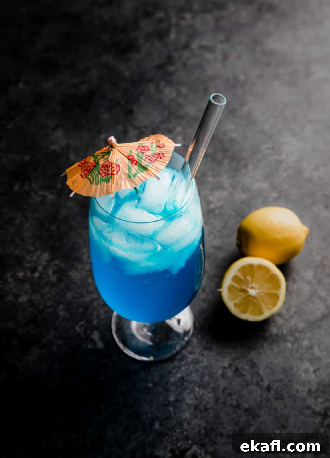 Γαλάζια Λιμνοθάλασσα Παρθένο Κοκτέιλ 8 Ένα Blue Lagoon Mocktail σε μαύρο φόντο με ένα λεμόνι δίπλα στο ποτήρι.