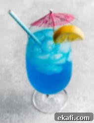 Γαλάζια Λιμνοθάλασσα Παρθένο Κοκτέιλ 9 Ένα Blue Lagoon Mocktail σε ένα μεγάλο γυάλινο ποτήρι με μια ροζ ομπρελίτσα και μια φέτα λεμονιού στο χείλος.