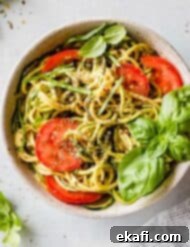 Fluted Zucchetti 8 Zucchetti Pasta in a white bowl with nutritional yeast sauce, fresh tomatoes, and basil garnish.