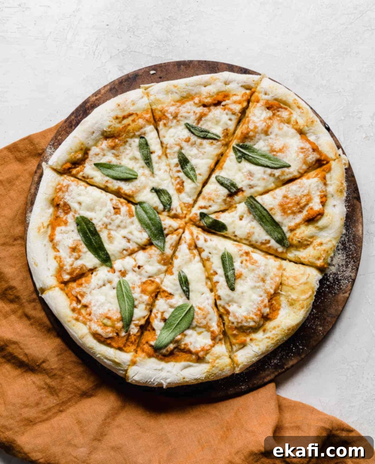 Harvest Moon Pizza 9 A beautifully baked pumpkin pizza, generously topped with crispy sage leaves, resting on a round pizza stone against a rustic gray background.