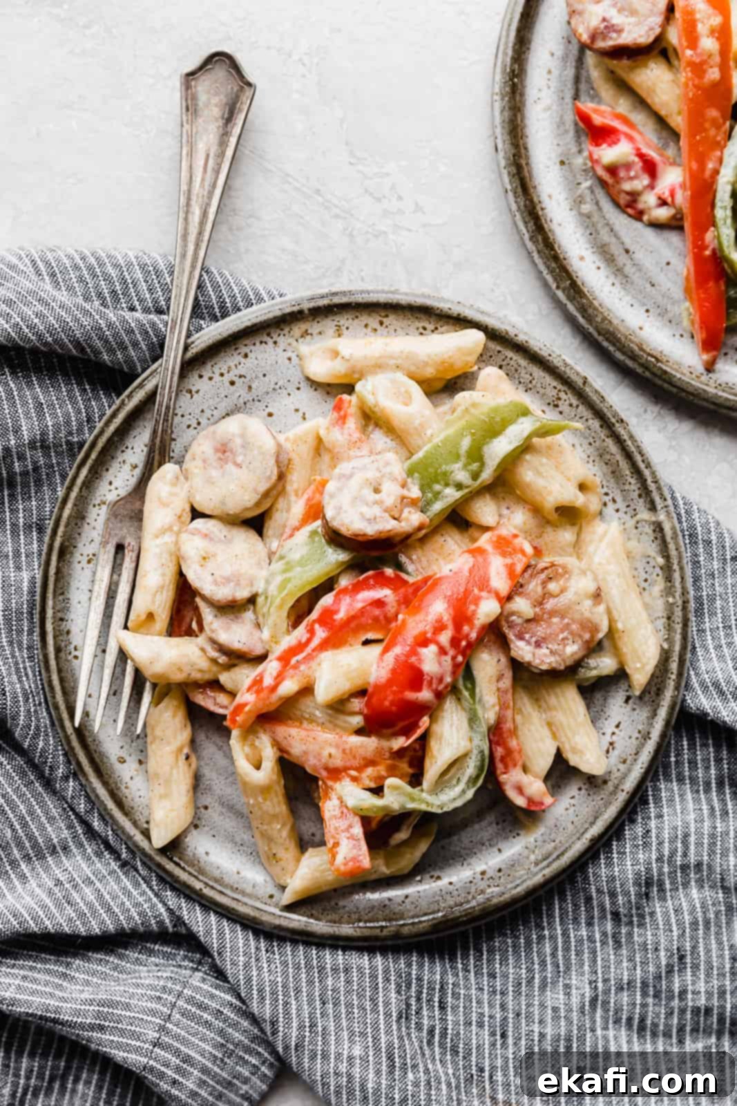 Spicy Cajun Sausage Pasta 2 A close-up of delicious Cajun Sausage Pasta, featuring perfectly cooked pasta, sliced red and green bell peppers, and savory Andouille sausage, all coated in a rich, creamy Cajun sauce on a gray plate, ready to be enjoyed.