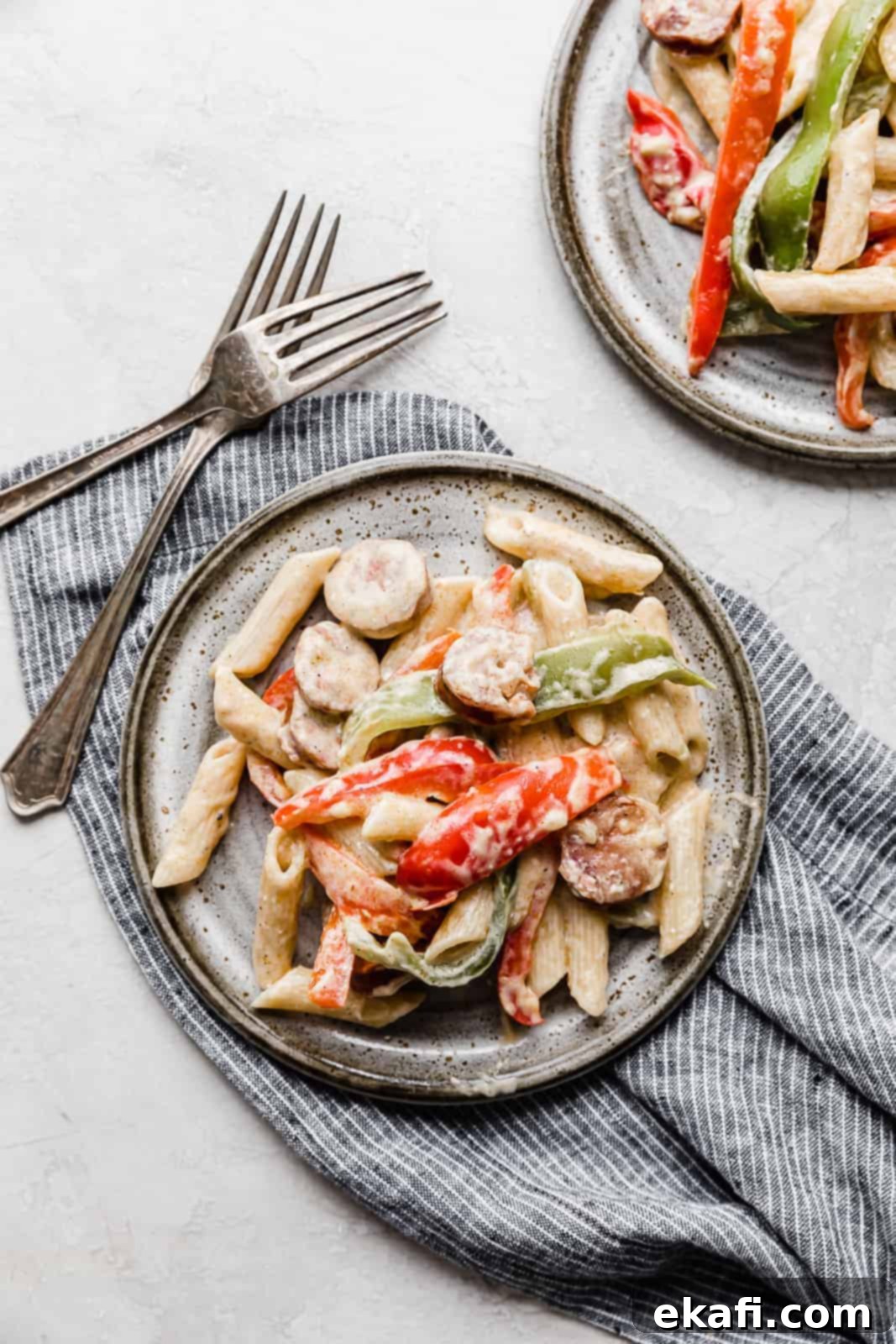 Spicy Cajun Sausage Pasta 11 A perfectly plated serving of creamy Cajun Sausage Pasta on a gray plate, with two silver forks resting to the left, highlighting the rich sauce, colorful peppers, and savory sausage.