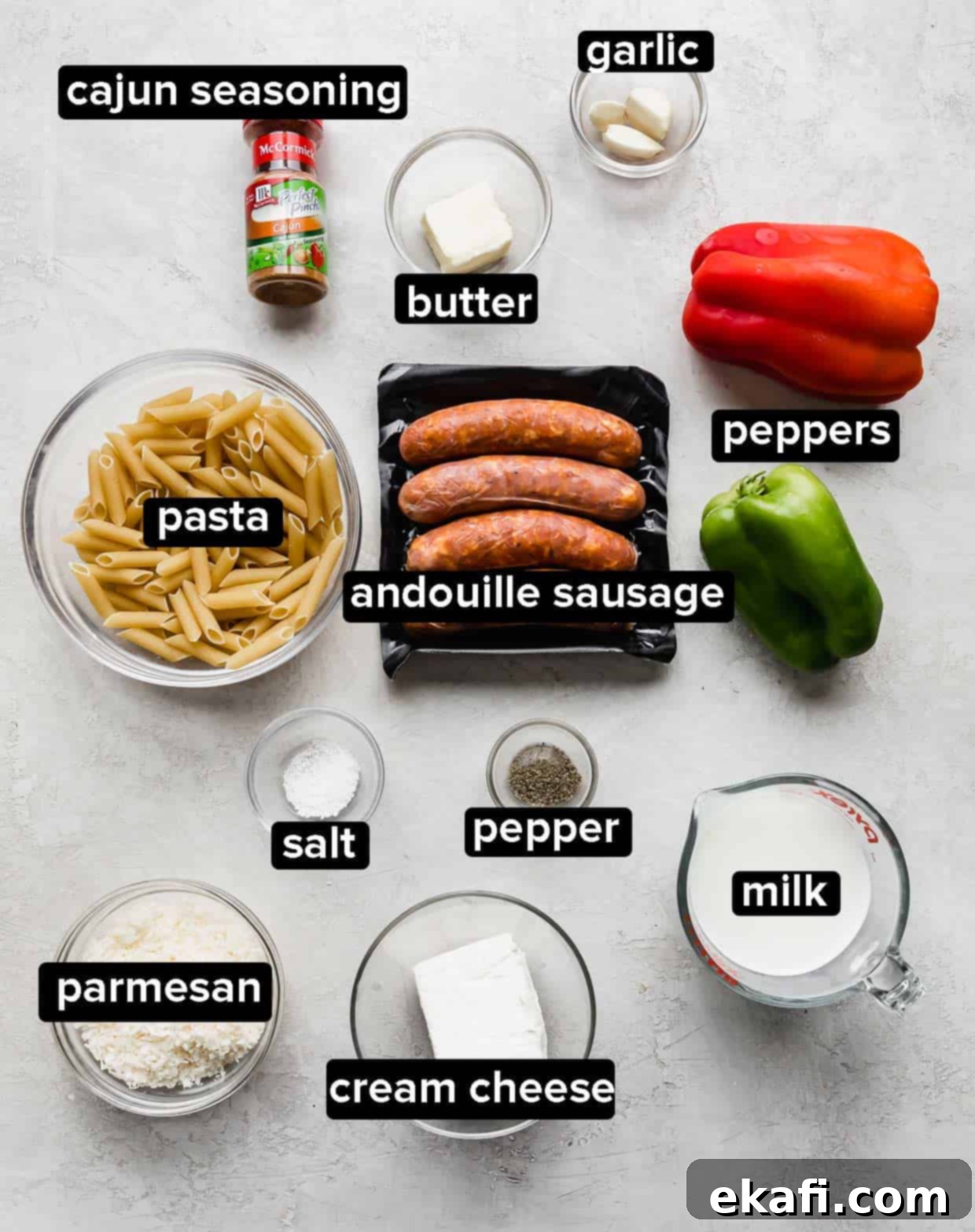 Spicy Cajun Sausage Pasta 3 A selection of fresh ingredients laid out on a gray background, including sliced red and green bell peppers, garlic cloves, a block of cream cheese, a bottle of milk, a package of Andouille sausage, and a bowl of Cajun seasoning, all ready to be used for making Cajun Sausage Pasta.