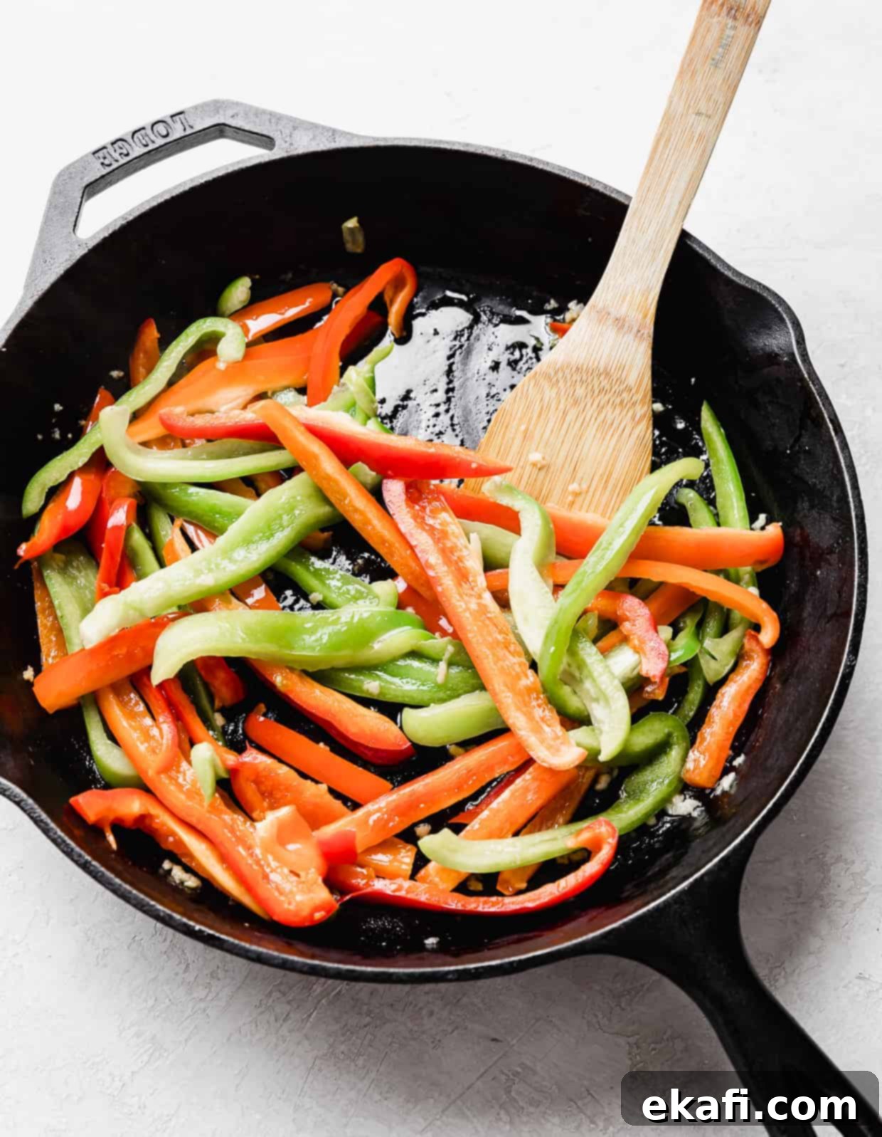 Spicy Cajun Sausage Pasta 4 A black skillet filled with vibrant, sliced red and green bell peppers, sizzling gently as they cook, forming the aromatic base for the Cajun Sausage Pasta.