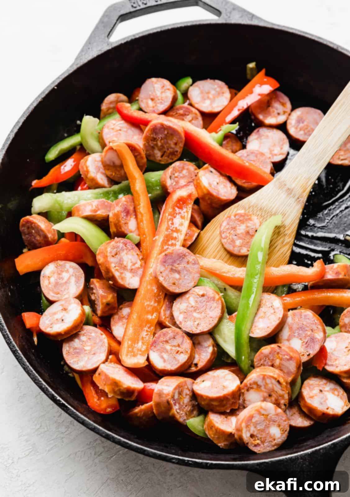 Spicy Cajun Sausage Pasta 5 A black skillet showcasing colorful sliced red and green bell peppers alongside browned slices of smoky Andouille sausage, seasoned with Cajun spices, cooking together to develop deep flavors for the pasta dish.