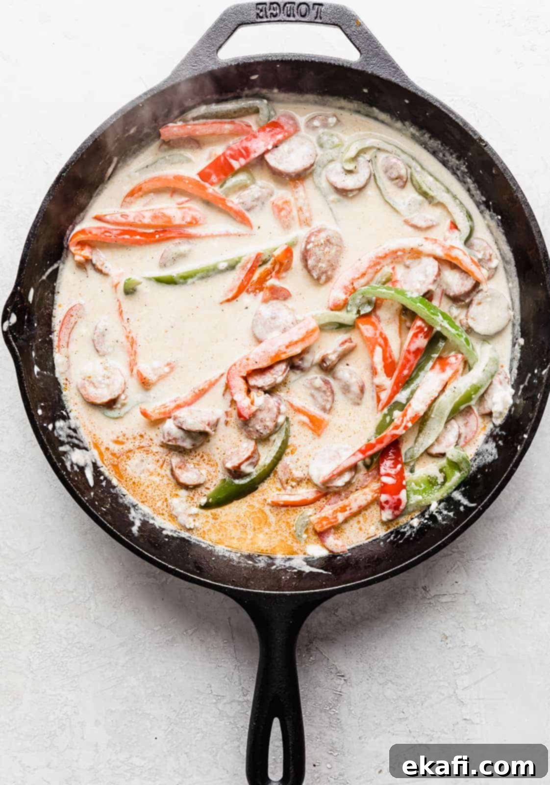 Spicy Cajun Sausage Pasta 7 A black skillet filled with sliced peppers and savory sausage, now bathed in a rich, smooth, and creamy white Cajun sauce, demonstrating the perfect consistency before adding the pasta.