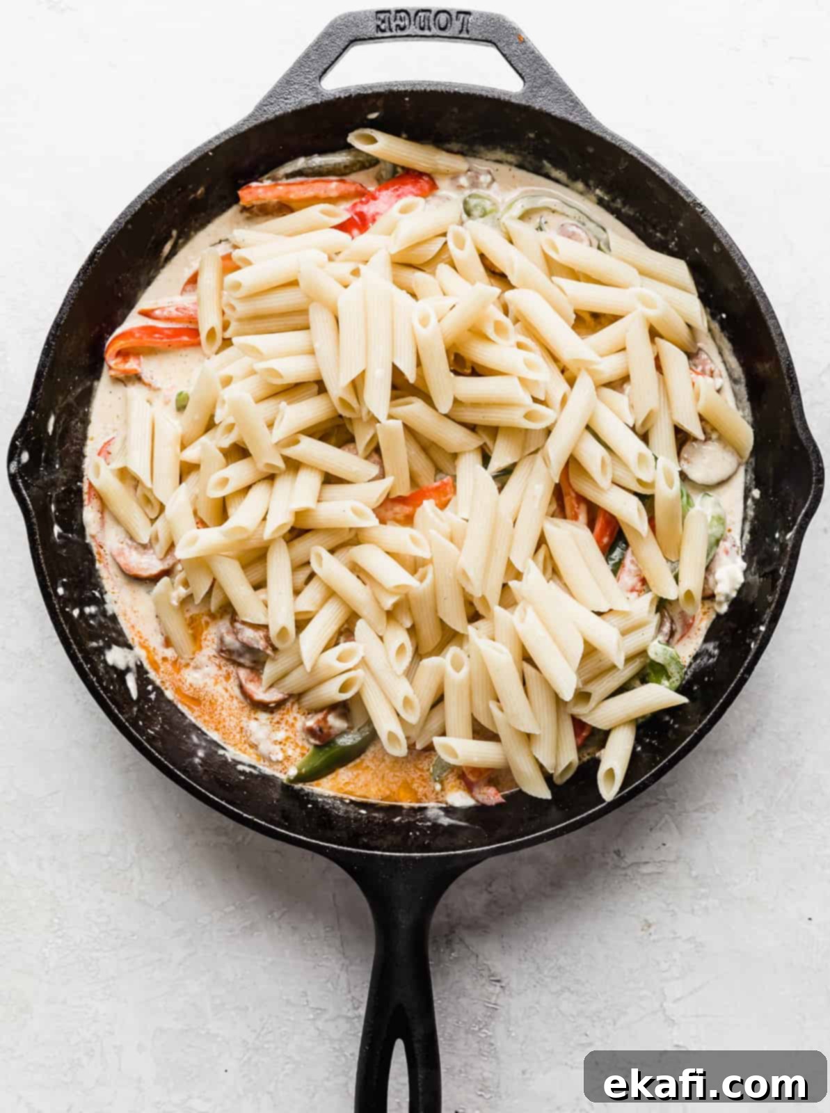 Spicy Cajun Sausage Pasta 8 Perfectly cooked penne pasta added to a black skillet, resting atop the creamy Cajun Sausage Pasta sauce, ready to be tossed and combined for a delectable meal.